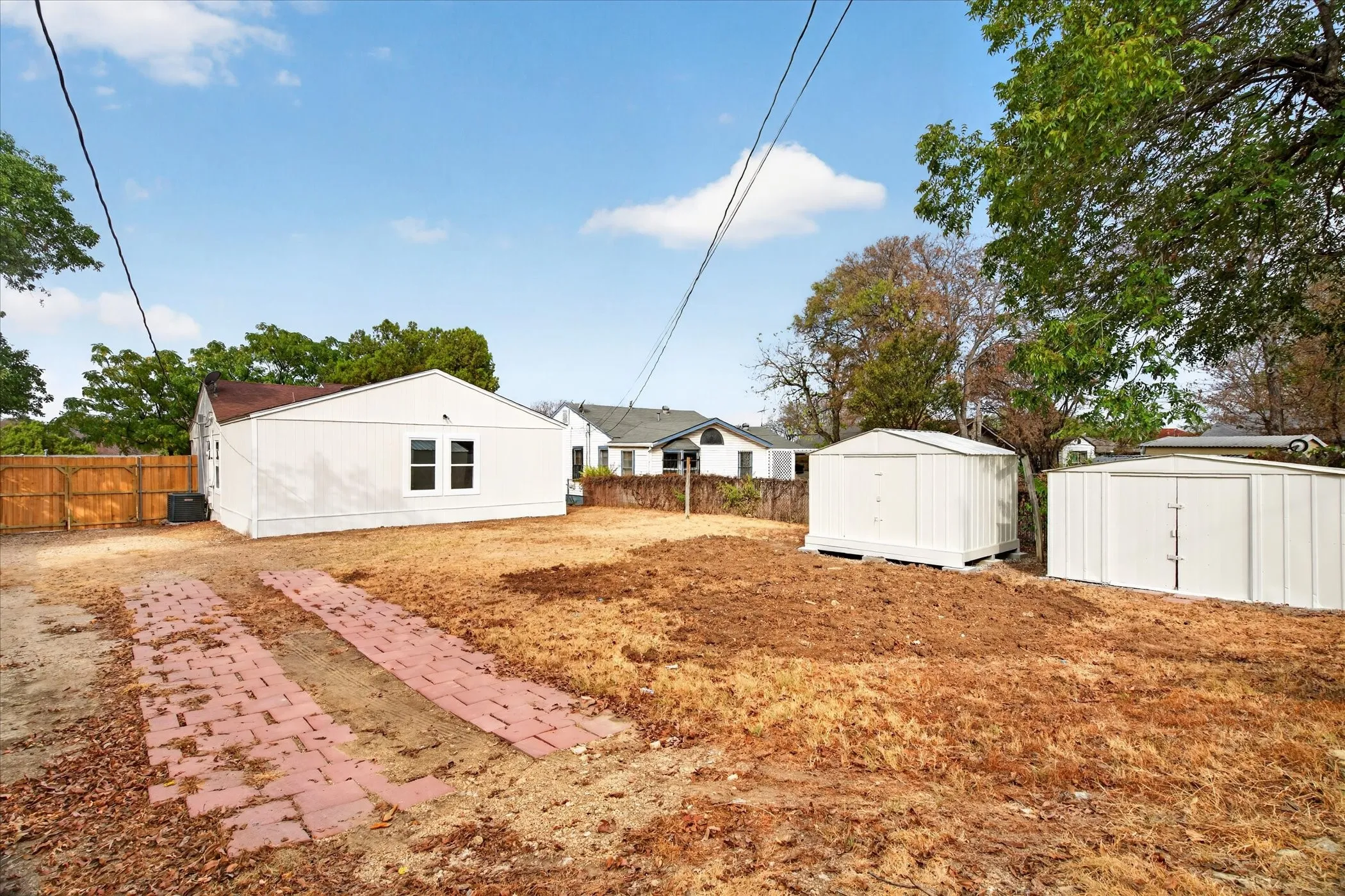 Expansive exterior with a white-sided structure, dual storage sheds, a wood privacy fence, and a brick paver pathway