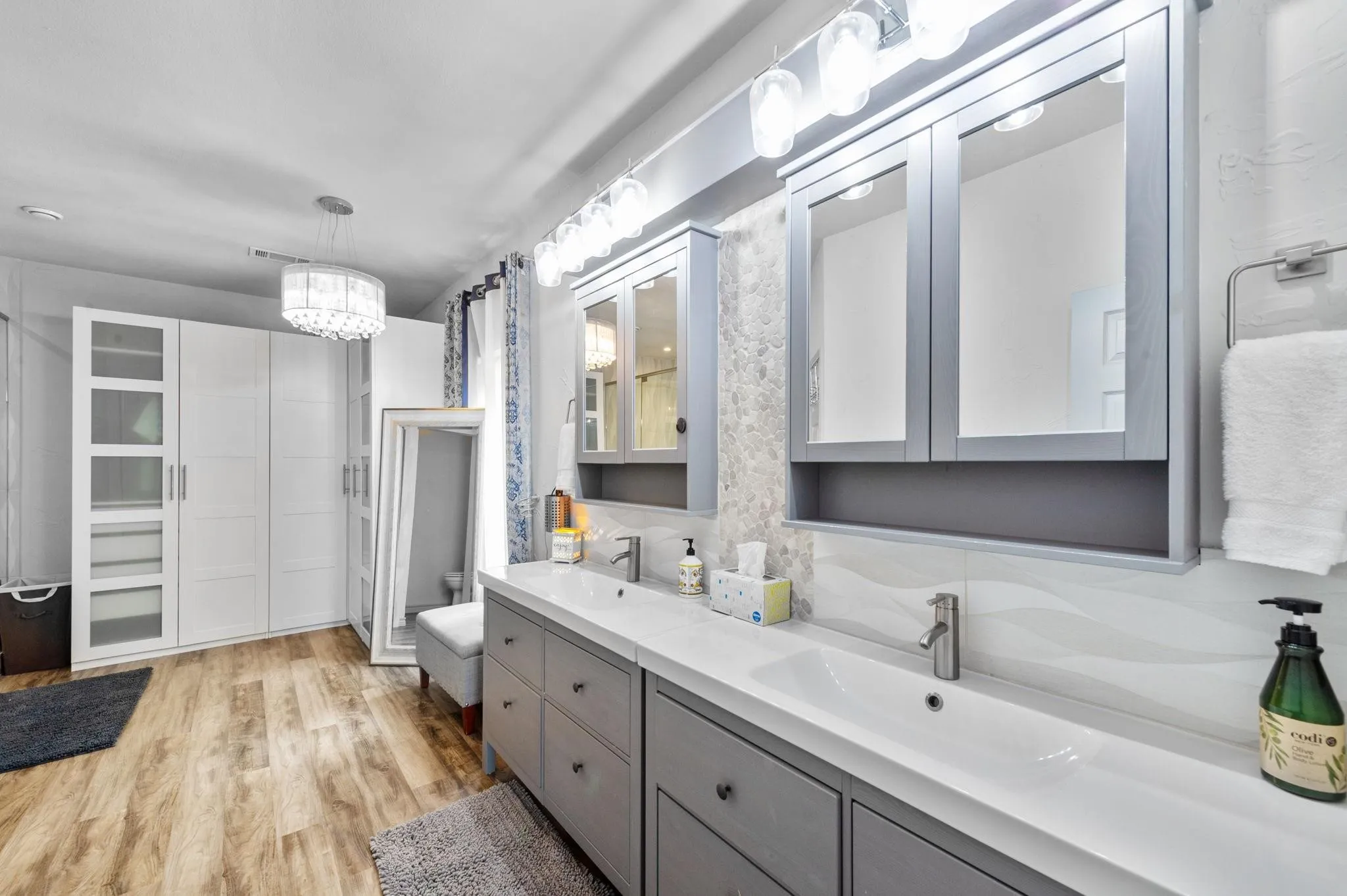 Double vanity with undermount sinks, wood-finish flooring, recessed medicine cabinets, contemporary lighting fixture, and floor-to-ceiling cabinetry