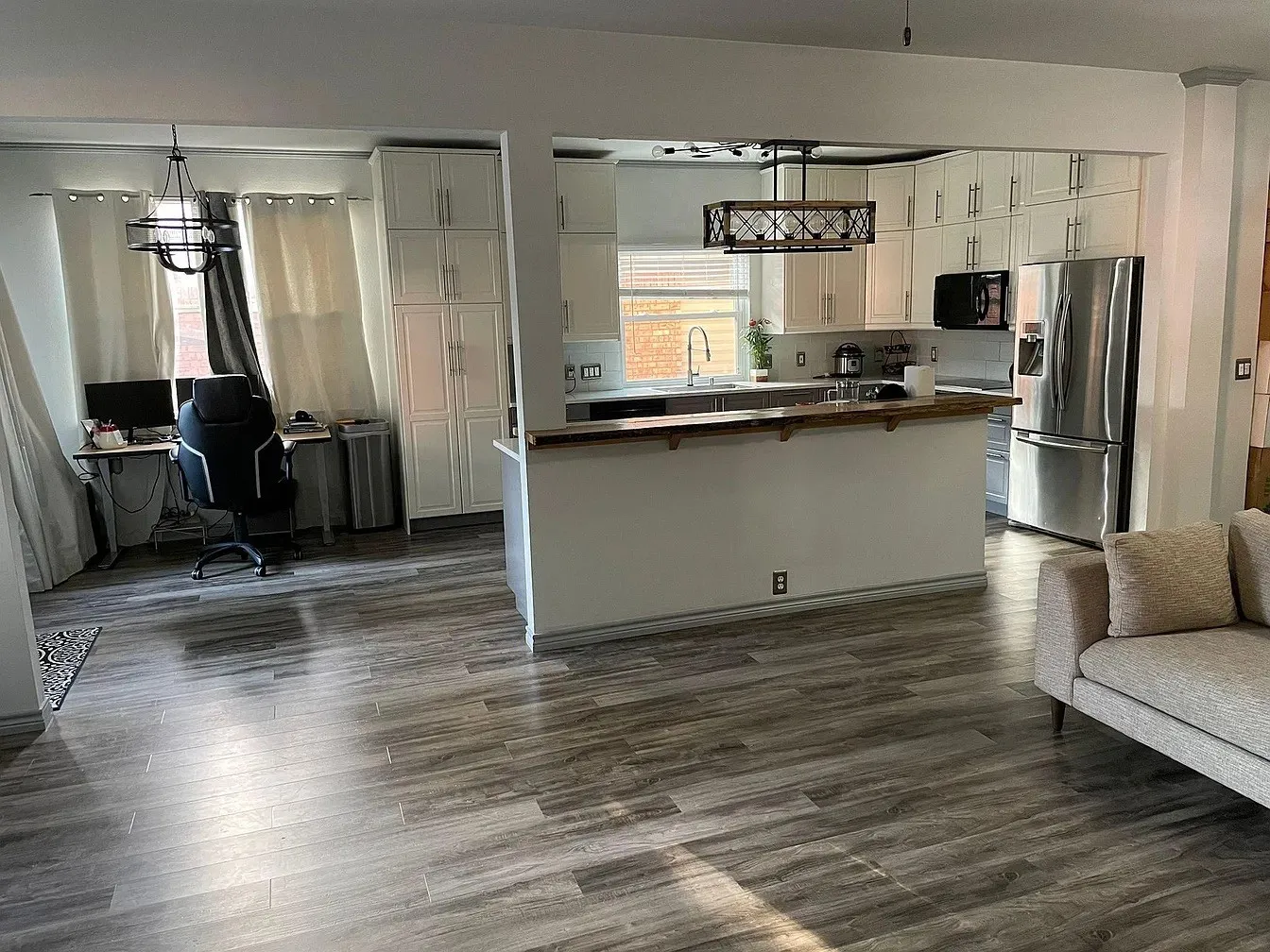 Wood-finish flooring throughout, kitchen with white upper and lower cabinetry, stainless steel appliances, and a wood-finish breakfast bar