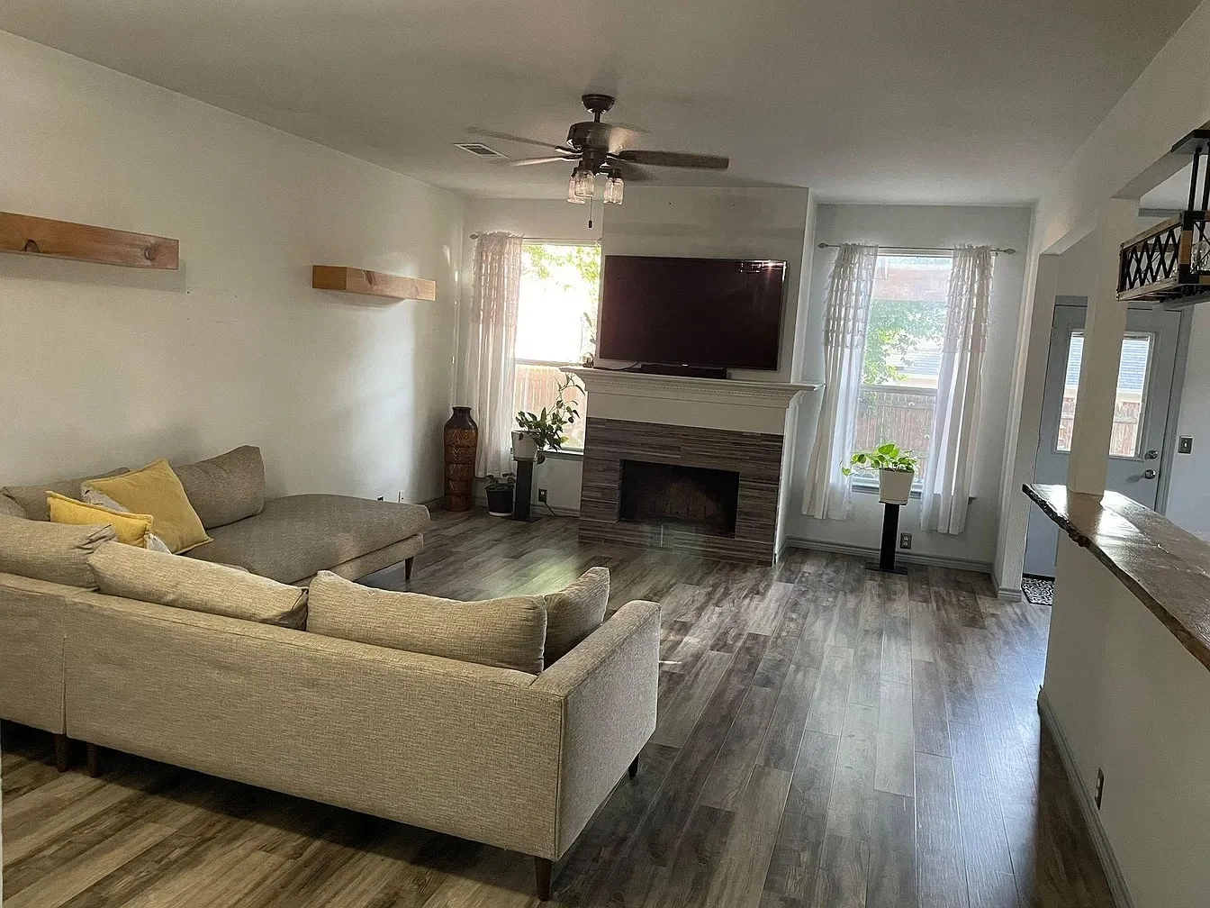 Living area featuring wood-finish flooring, a fireplace with a stone surround, and a ceiling fan