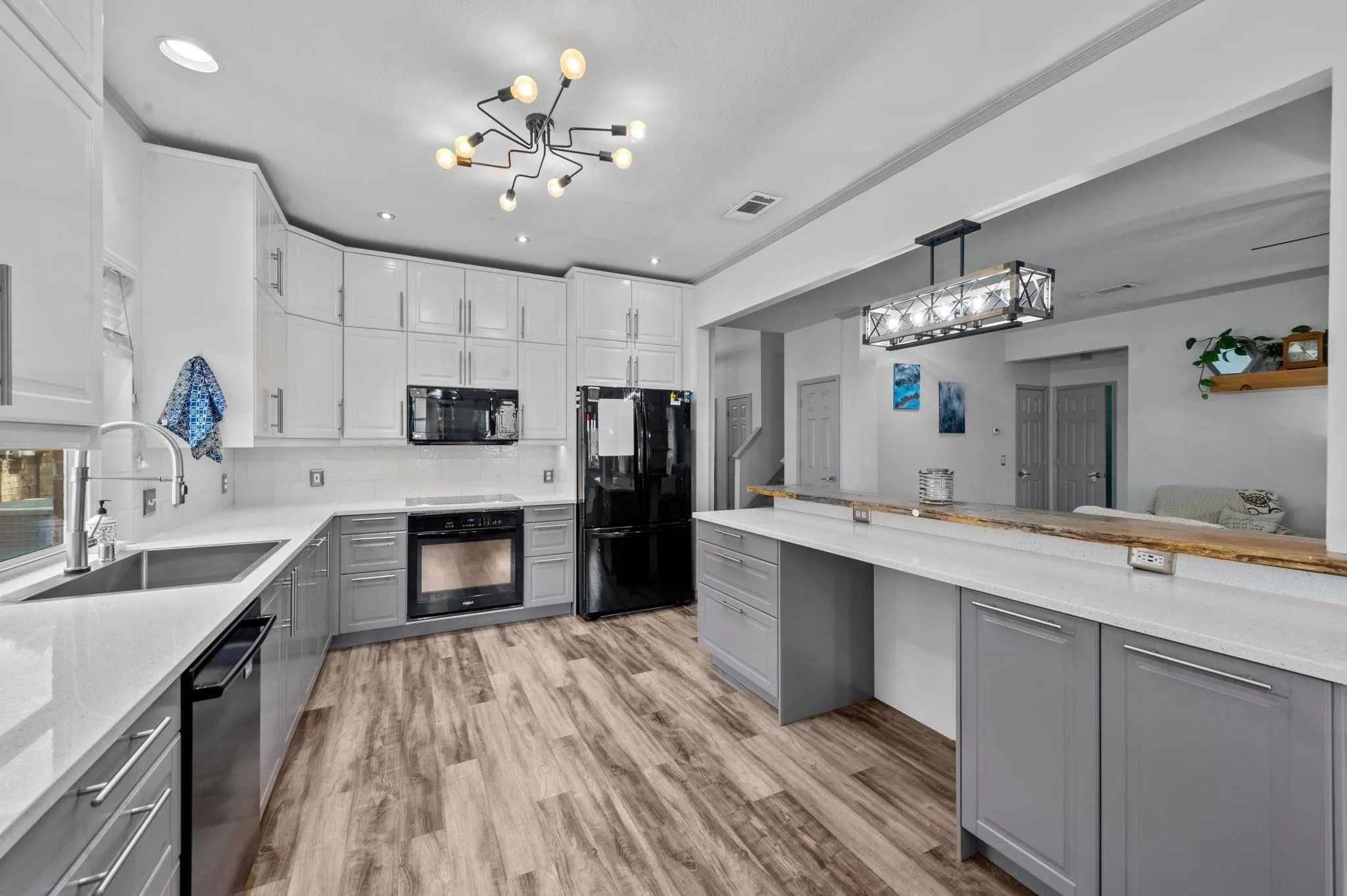 Two-tone cabinetry with white upper cabinets and gray lower cabinets, wood-finish flooring, white countertops, built-in stainless steel sink, and built-in black appliances