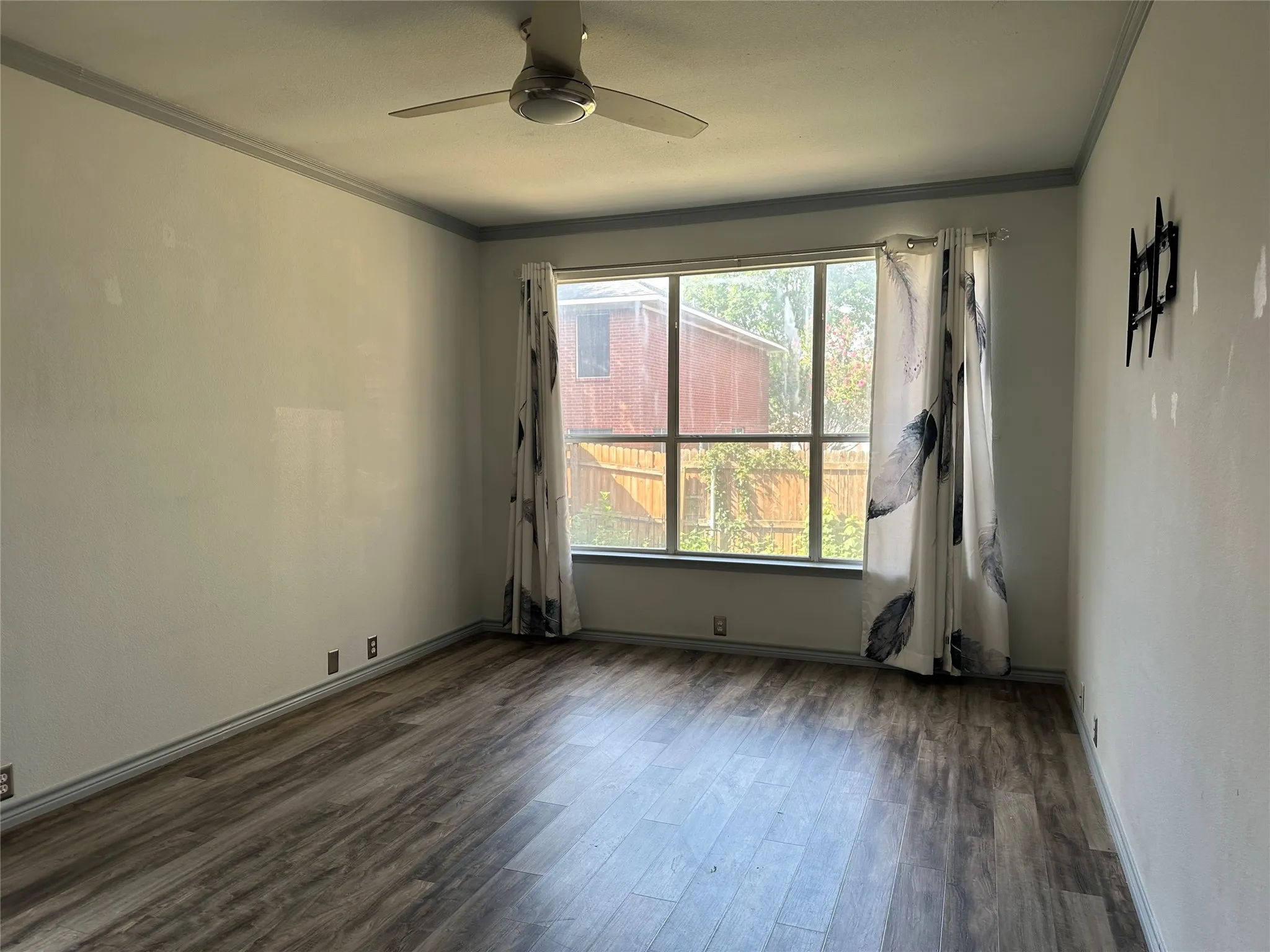 Spacious room featuring wood-finish flooring, a large multi-pane window, and a ceiling fan