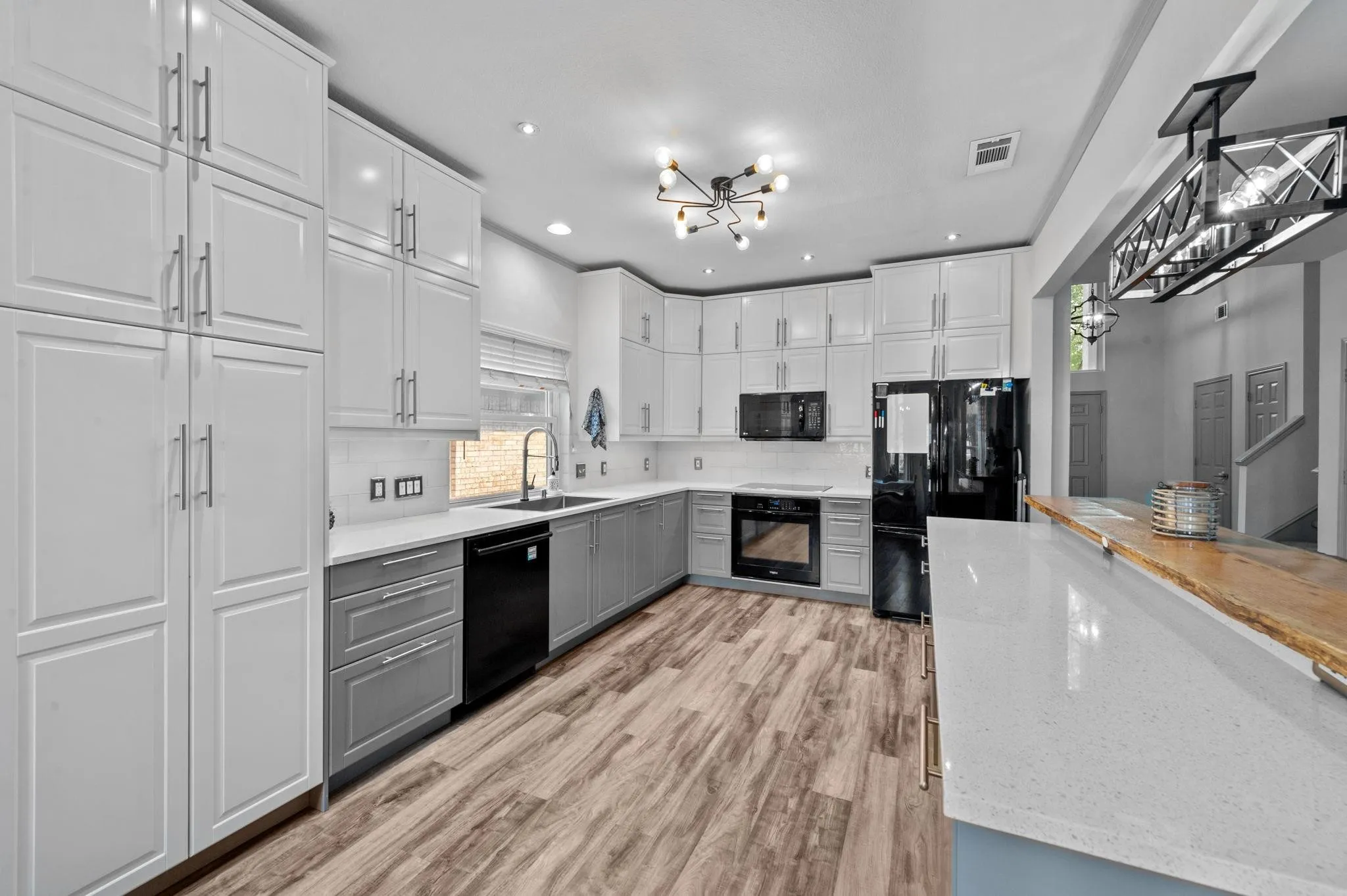 Modern kitchen featuring two-tone cabinetry, wood-finish flooring, recessed lighting, and a linear chandelier