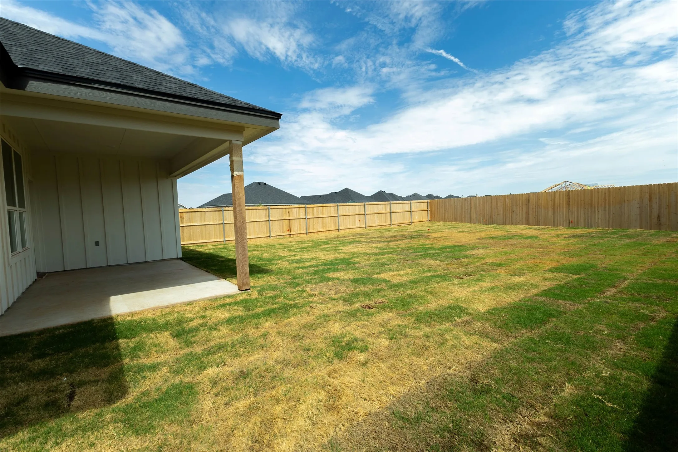 Expansive backyard featuring a covered patio, wood privacy fencing, and a shingled roofline
