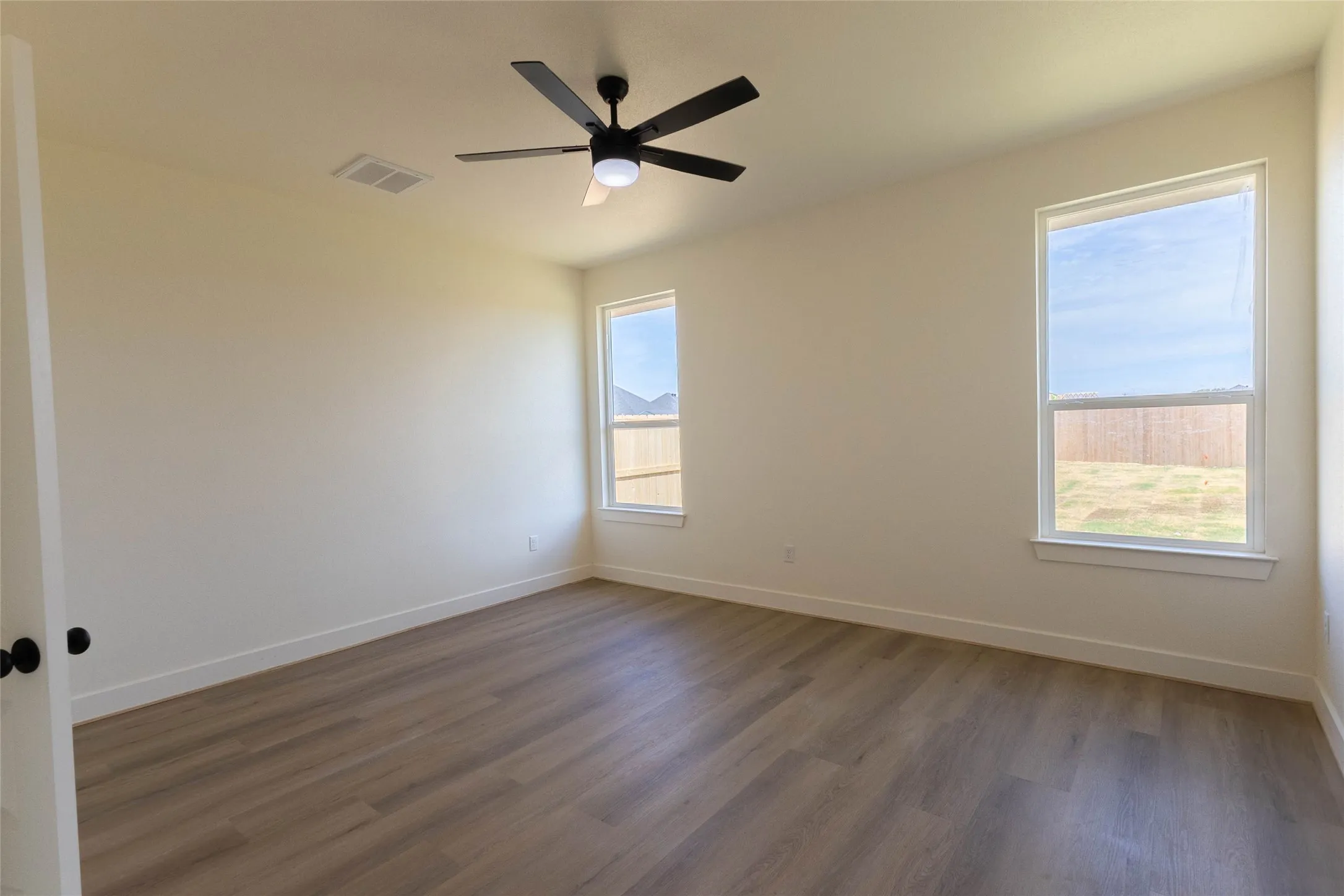 Wood-finish flooring, two windows, and a ceiling fan with integrated lighting