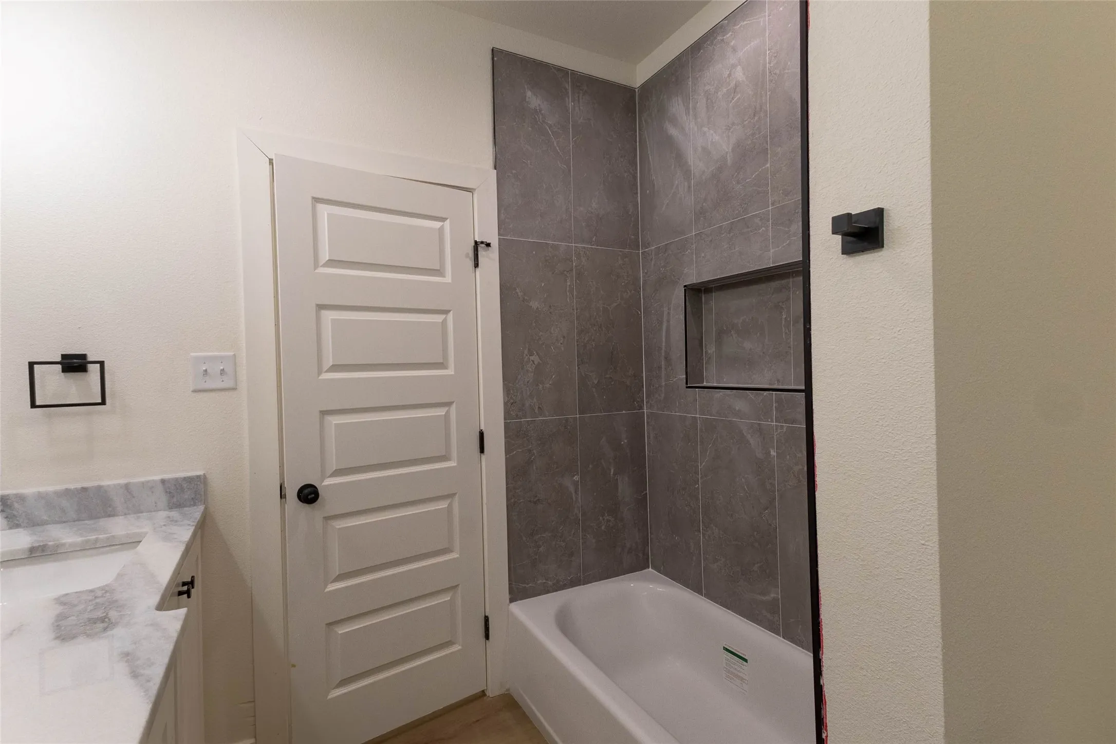 Built-in bathtub with subway tile surround, recessed shower niche, and matte black fixtures