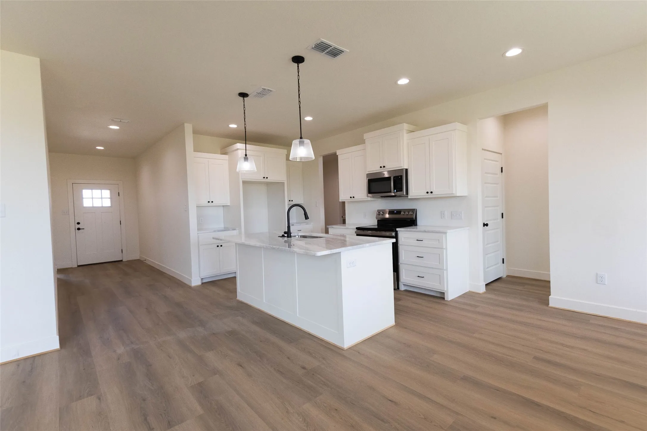 Well-appointed kitchen featuring white cabinetry, a central island with a sink, stainless steel appliances, pendant lighting, and wood-finish flooring