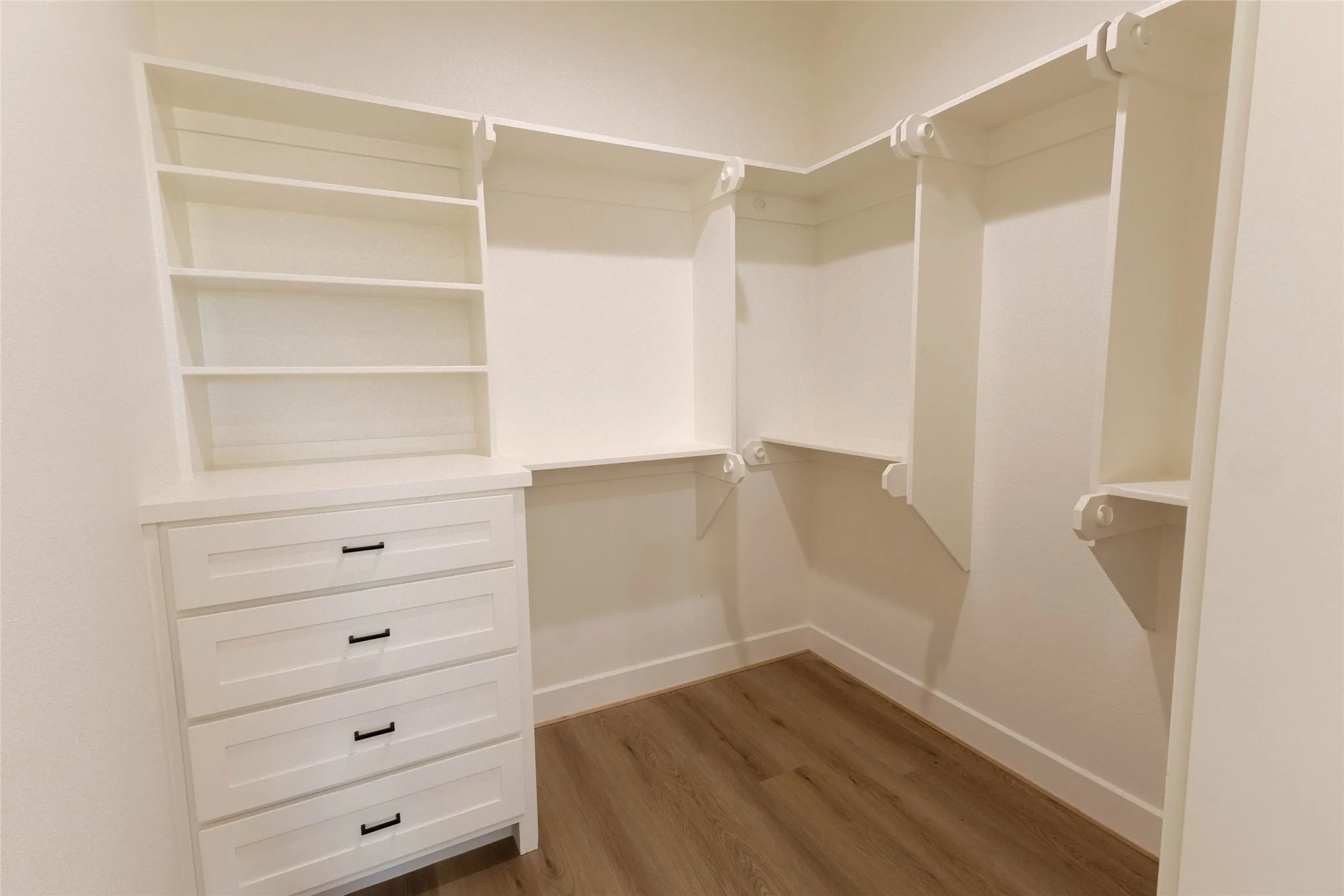 Built-in white shelving, integrated drawer storage with matte black hardware, and wood-finish flooring