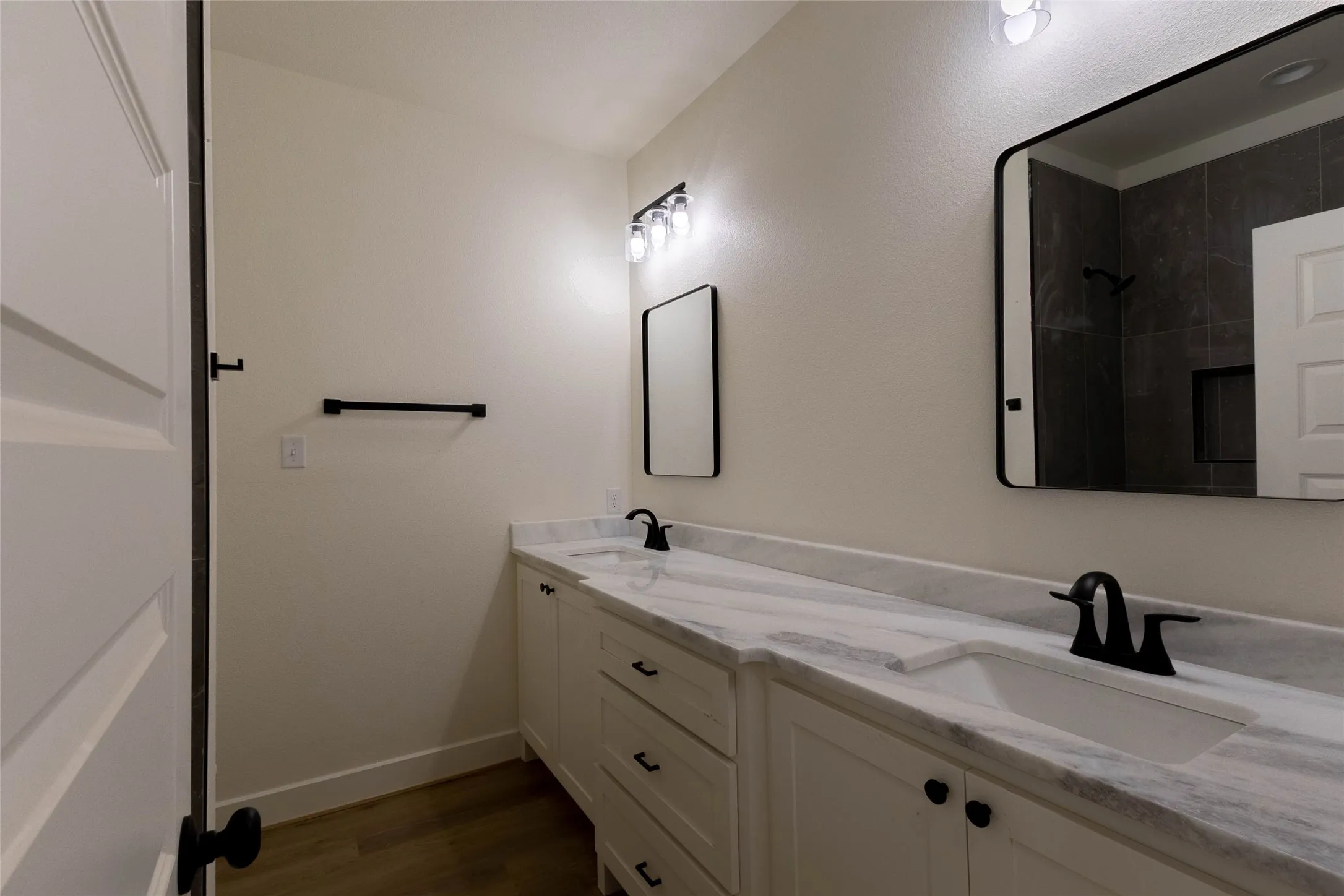 Double vanity with undermount sinks, stone countertops, matte black hardware, and wood-finish flooring