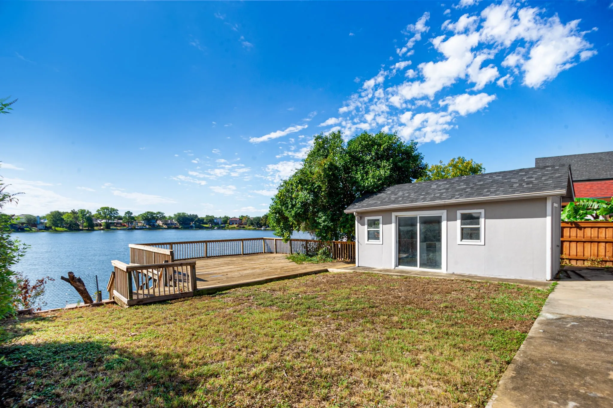 Waterfront property featuring a large wooden deck, a separate utility building with sliding glass doors, and a concrete pathway