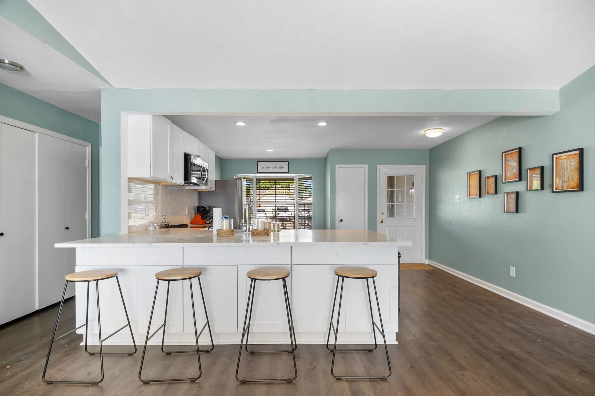 Kitchen island with light-toned countertop, white cabinetry, integrated stainless steel microwave, and wood-finish flooring