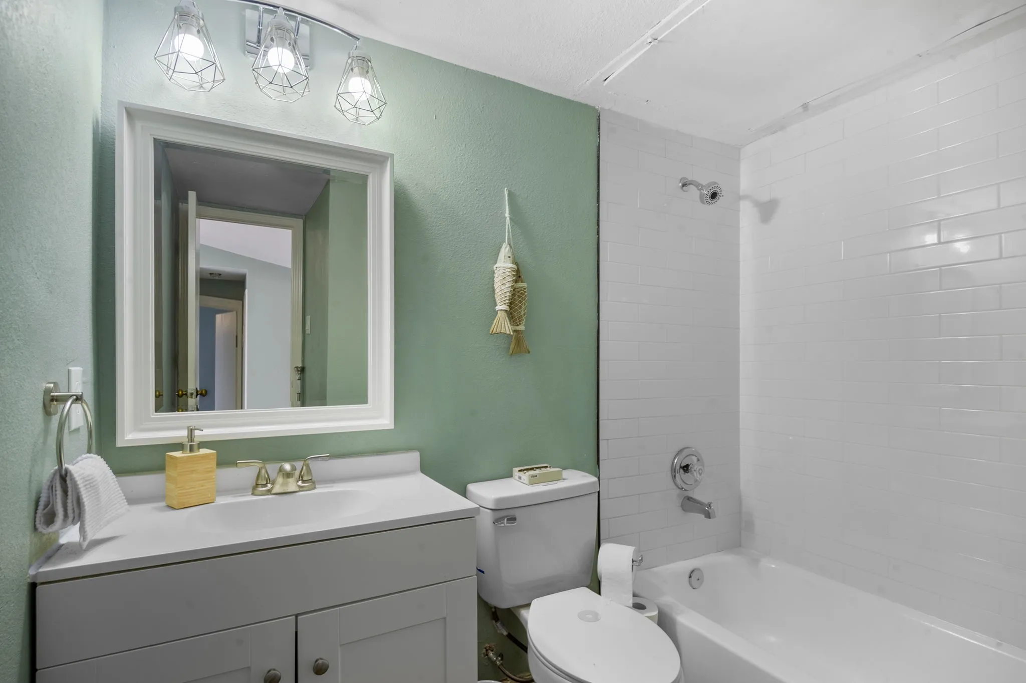 White vanity with integrated sink and brushed nickel faucet, framed mirror, three-light vanity fixture, white subway tile shower surround, and white bathtub