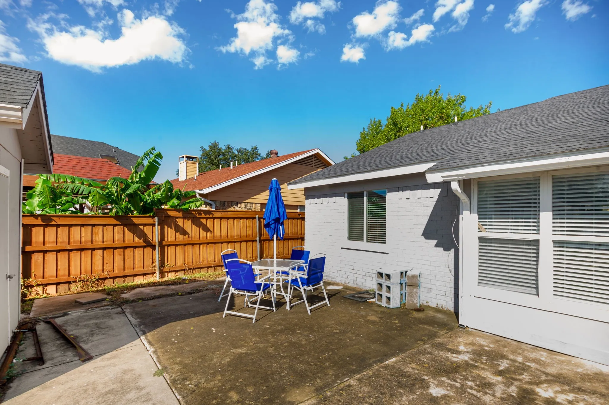 Private fenced yard with concrete patio, painted brick exterior, and dark shingle roofing