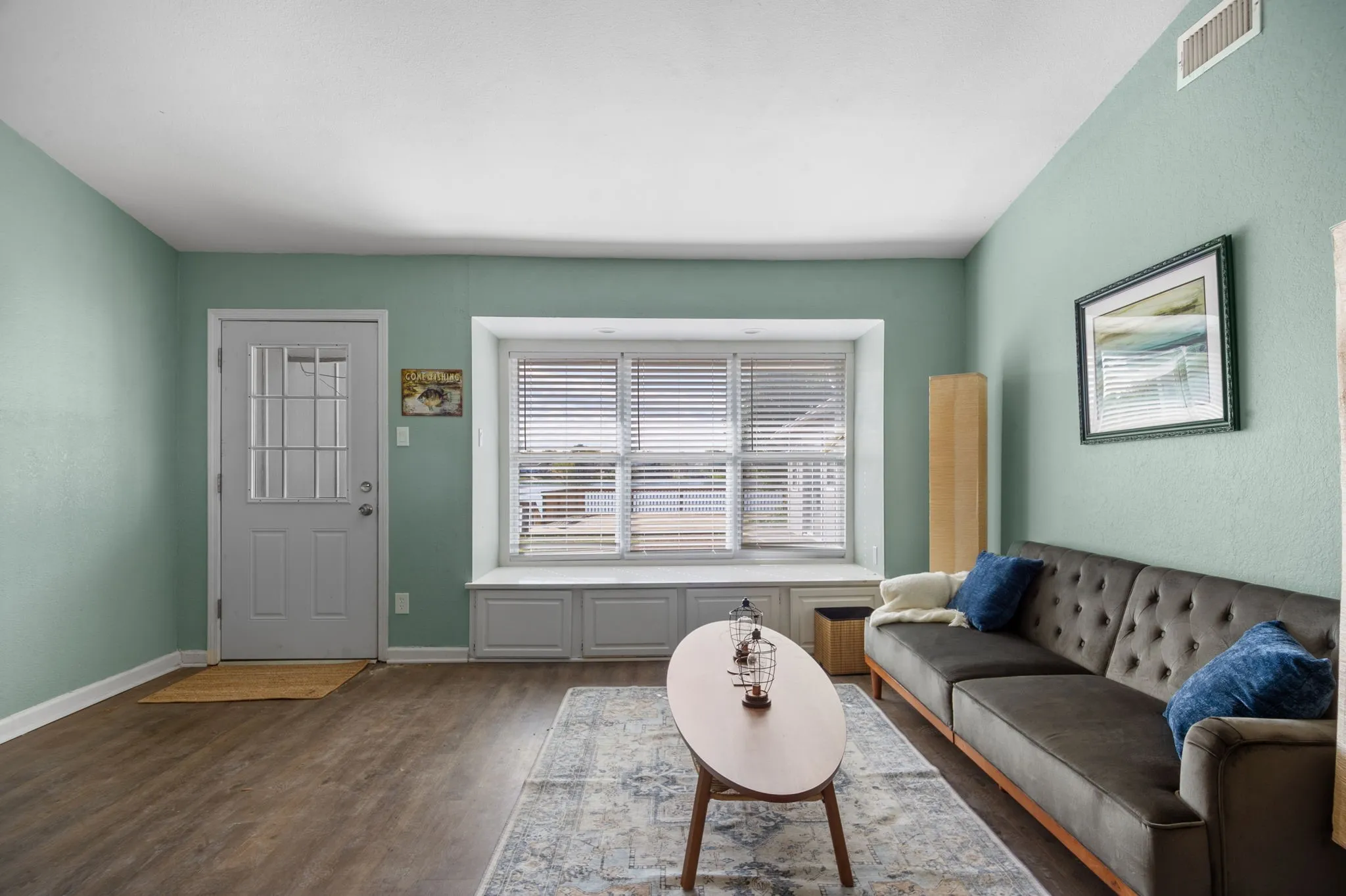 Wood-finish flooring, light green wall finishes, and a window with blinds and built-in storage
