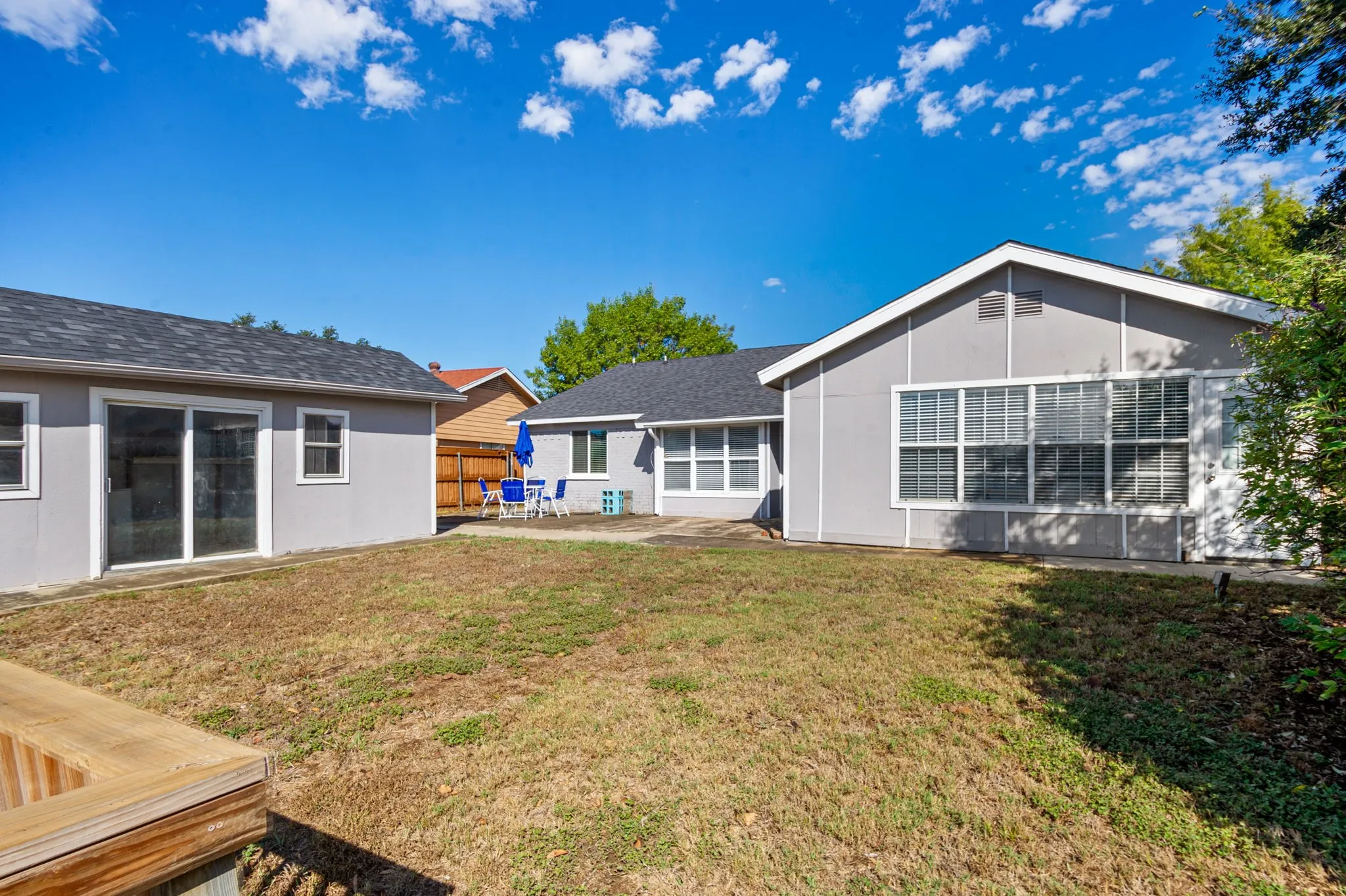 Backyard featuring a secondary structure with sliding glass doors, a main residence with multiple windows, and a wood-finish deck element