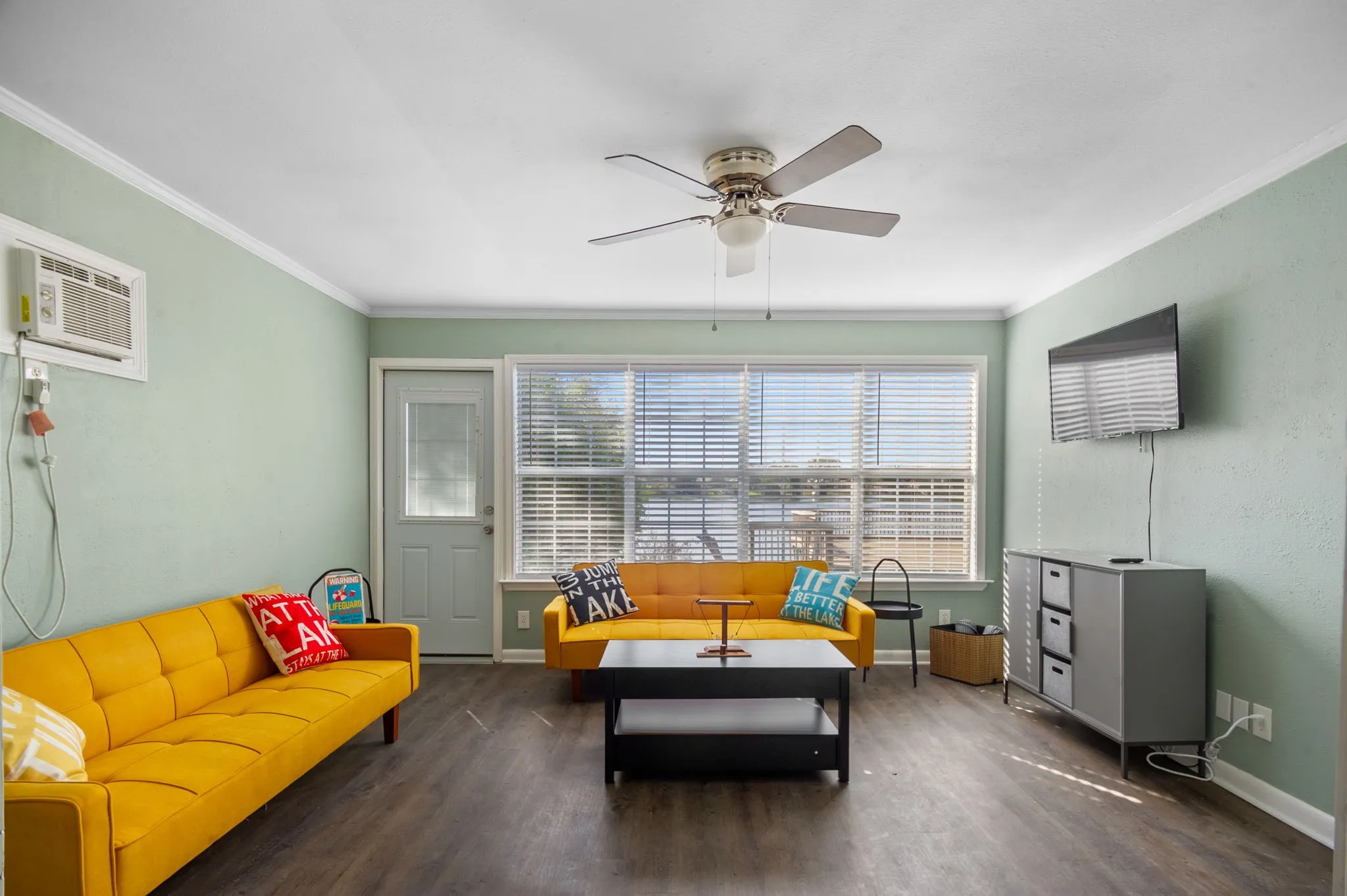 Expansive living area with wood-finish flooring, a ceiling fan, and large windows with blinds