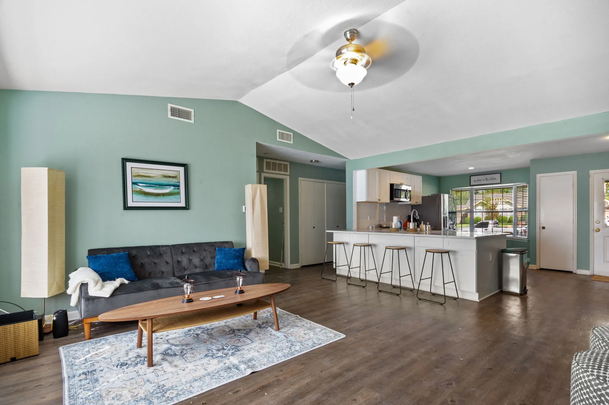 Vaulted ceiling, wood-finish flooring, kitchen island with seating, stainless steel appliances, and white cabinetry