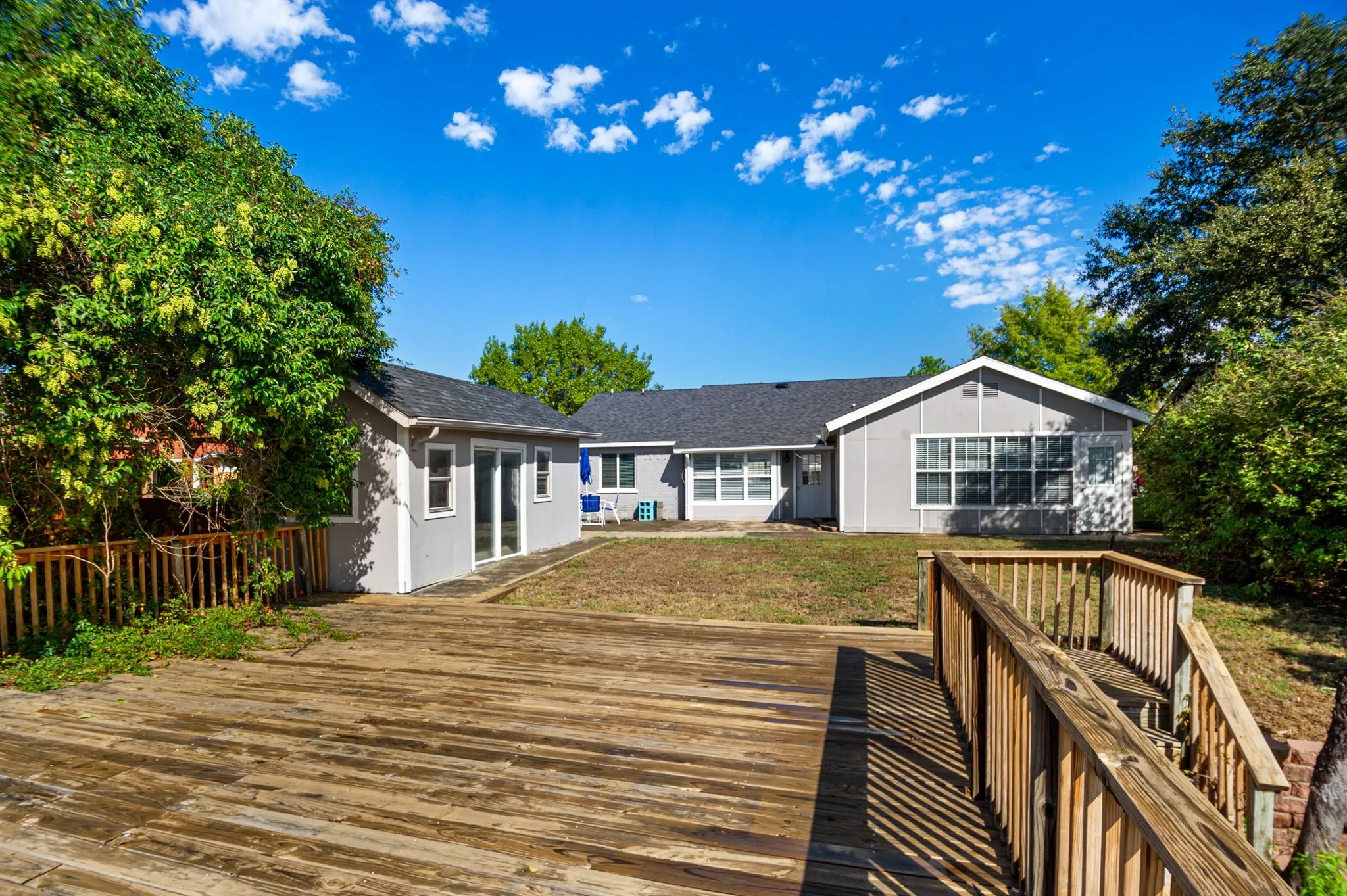 Expansive wooden deck with railing, detached structure with sliding glass doors, and a main residence featuring multiple windows