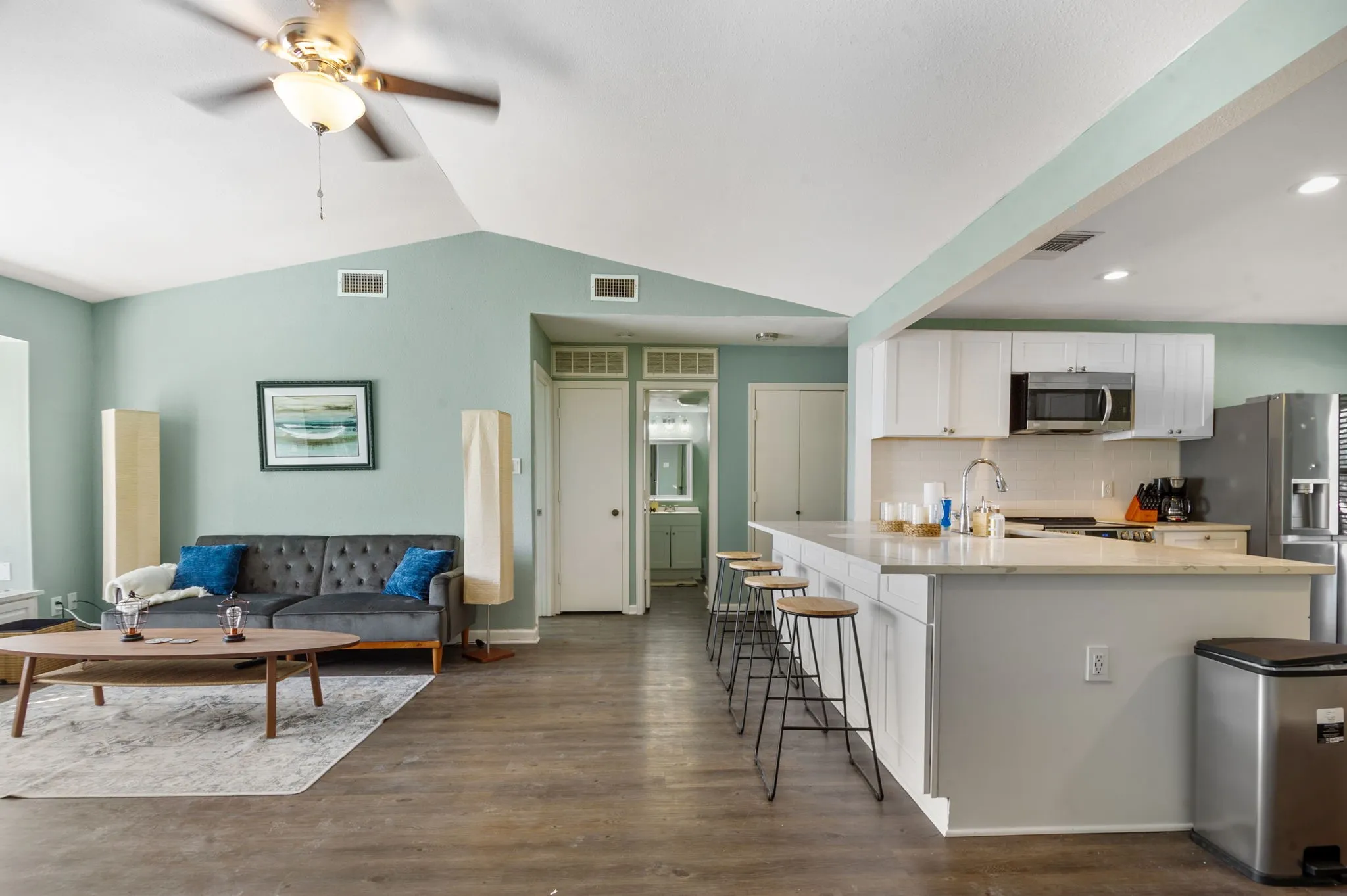 Vaulted ceilings with a ceiling fan, wood-finish flooring, white kitchen cabinetry, stainless steel appliances, and a kitchen island with seating