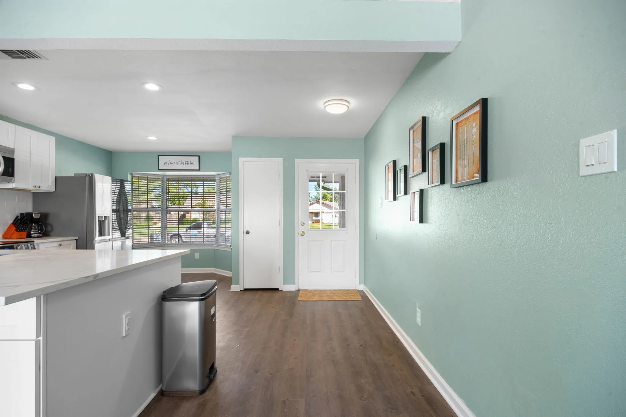 Wood-finish flooring, recessed lighting, bay window, white paneled door, and white trim