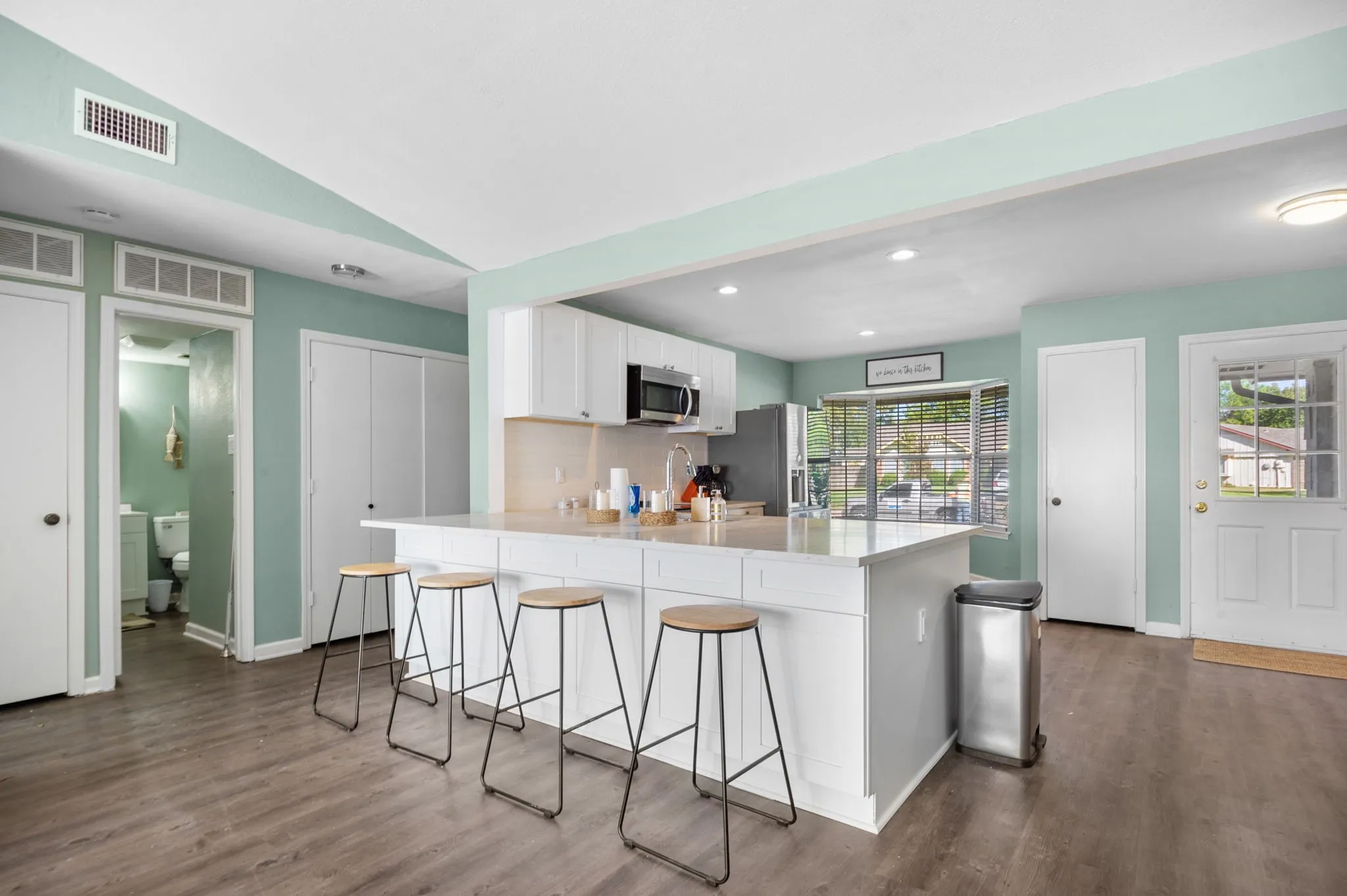 Kitchen featuring white cabinetry, a large kitchen island with counter seating, stainless steel appliances, wood-finish flooring, and a large window