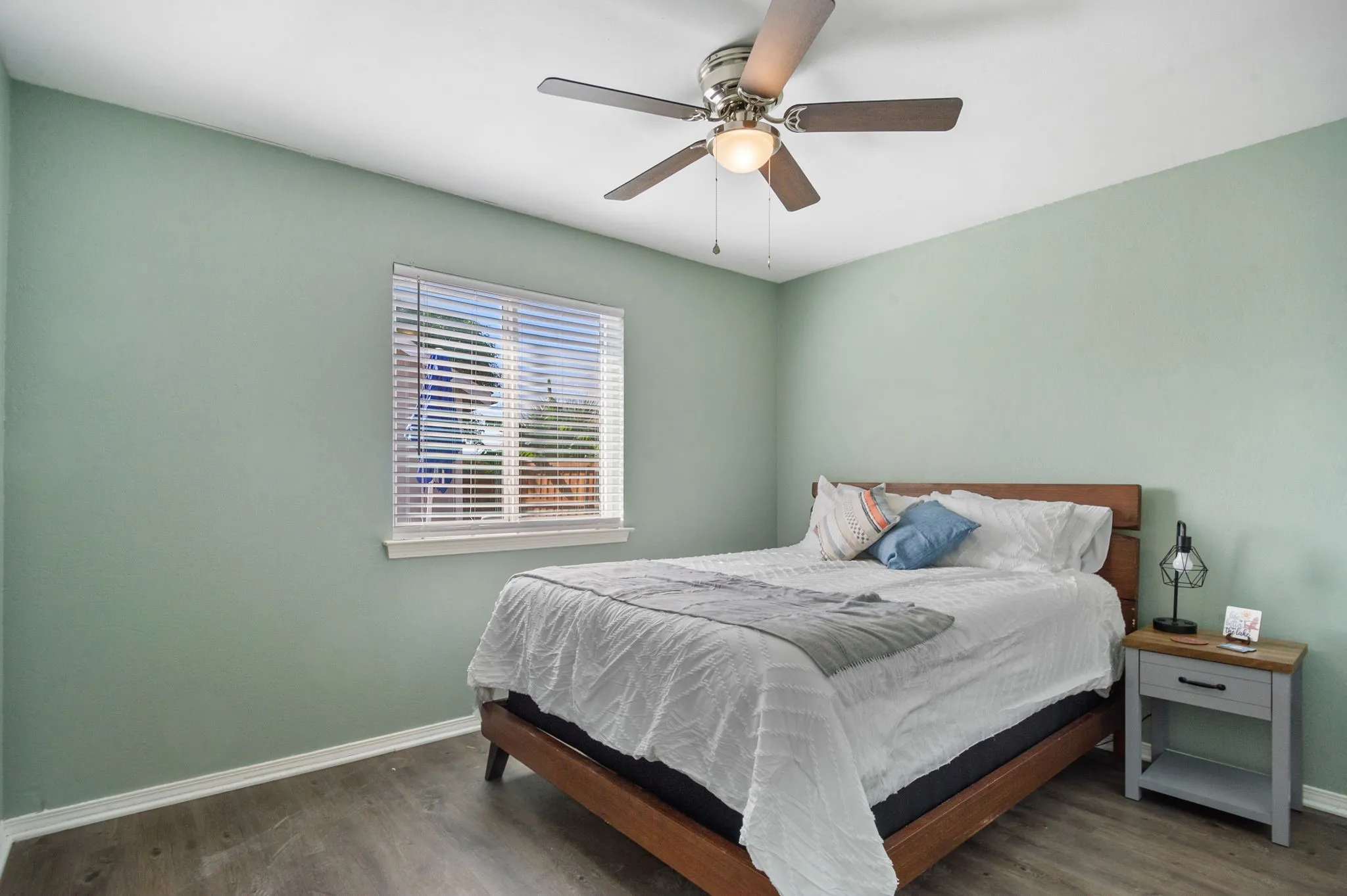 Wood-finish flooring, ceiling fan with integrated lighting, window with blinds, and light-toned wall paint