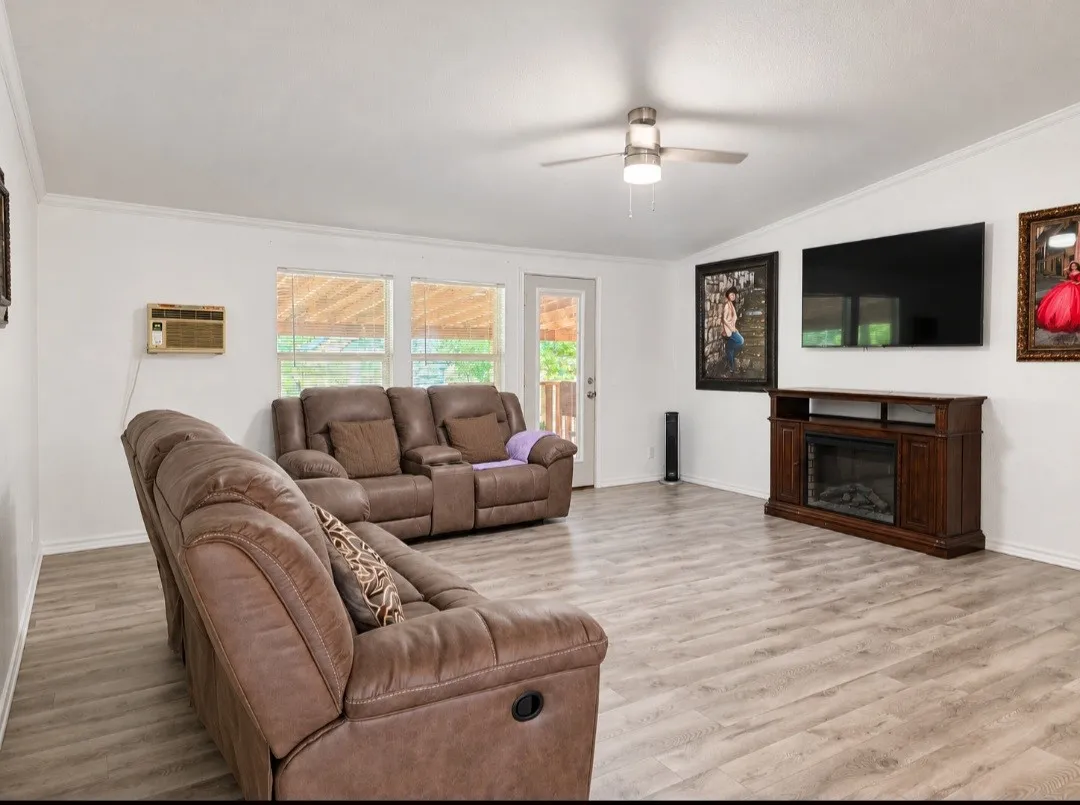 Wood-finish flooring throughout, white walls, and a ceiling fan with integrated lighting