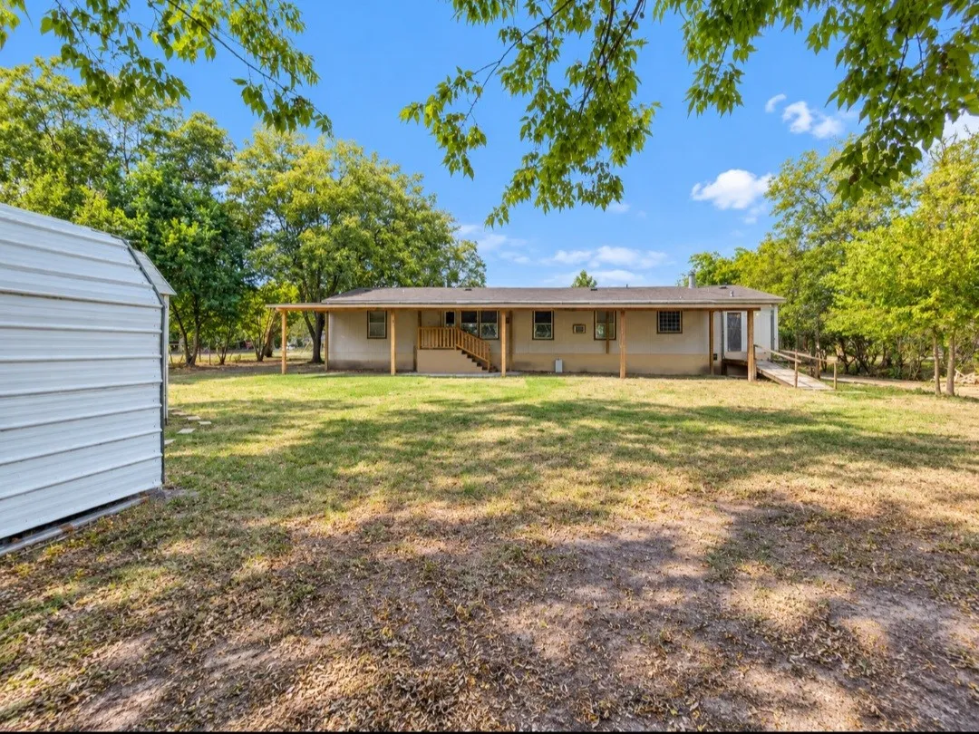 Expansive backyard featuring a covered patio, wooden deck with stairs, and a separate storage shed