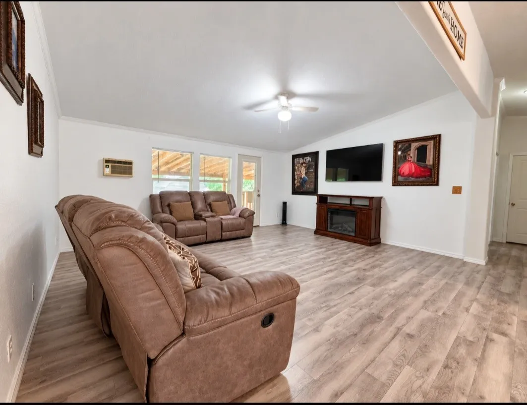 Spacious room featuring light wood-finish flooring, white walls, and a ceiling fan with light fixture