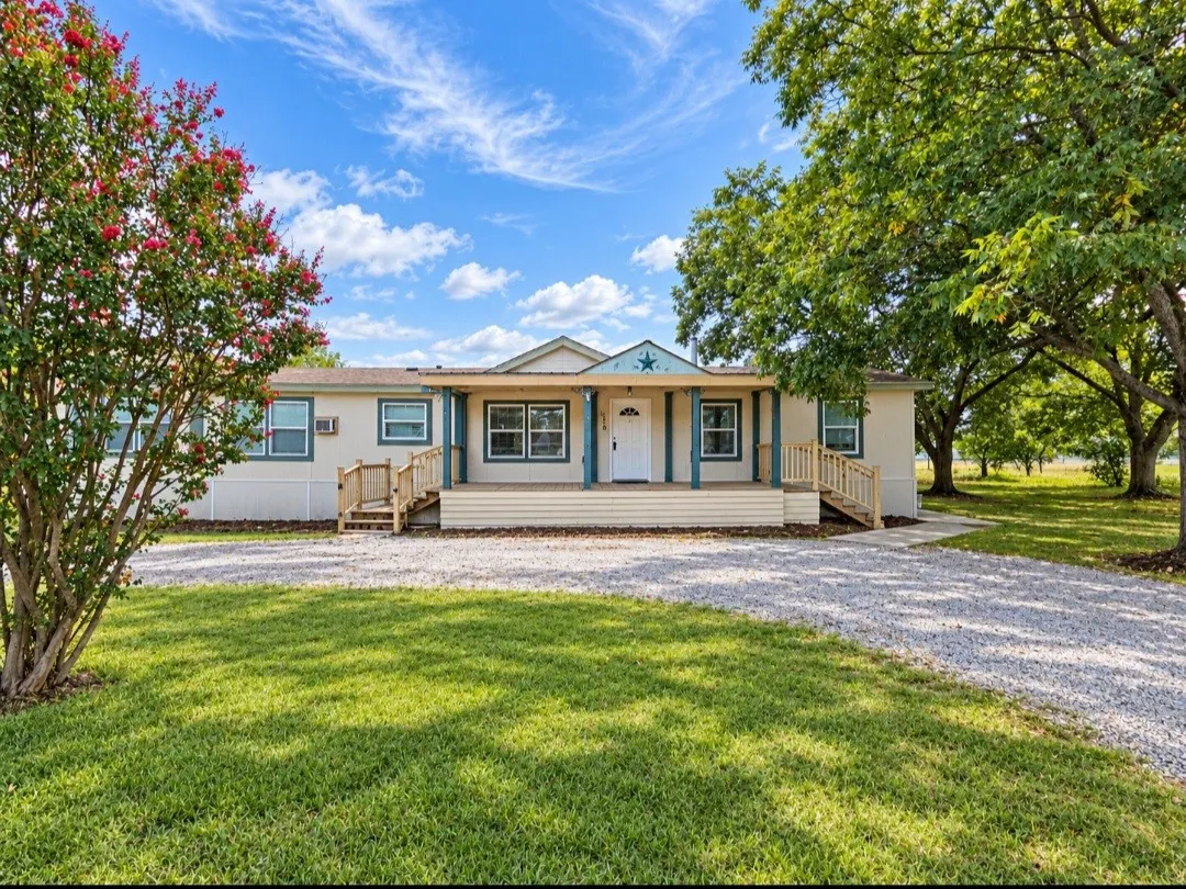 Expansive gravel driveway, mature trees, and a covered front porch with steps and railings