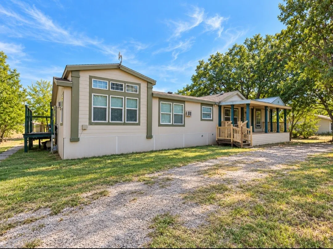 Gravel driveway leading to a residence with a covered porch, wood-framed windows, and a raised exterior deck