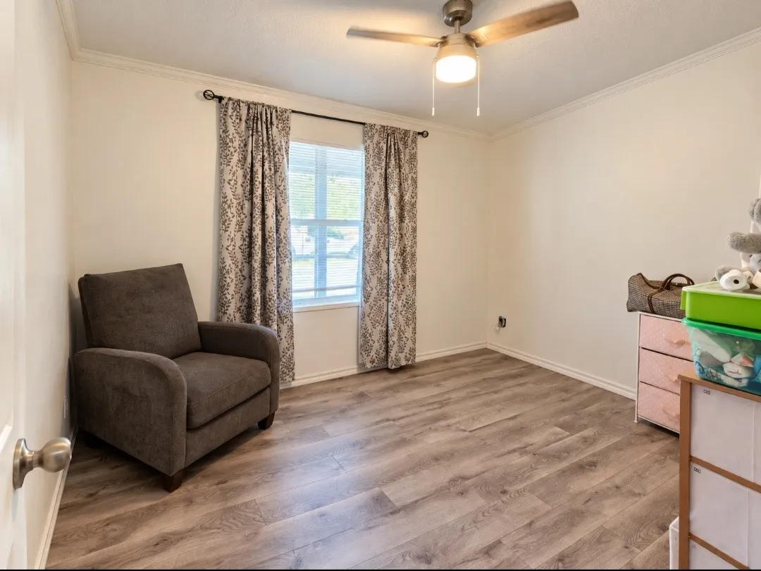 Wood-finish flooring, crown molding, ceiling fan with light fixture, and window with blinds