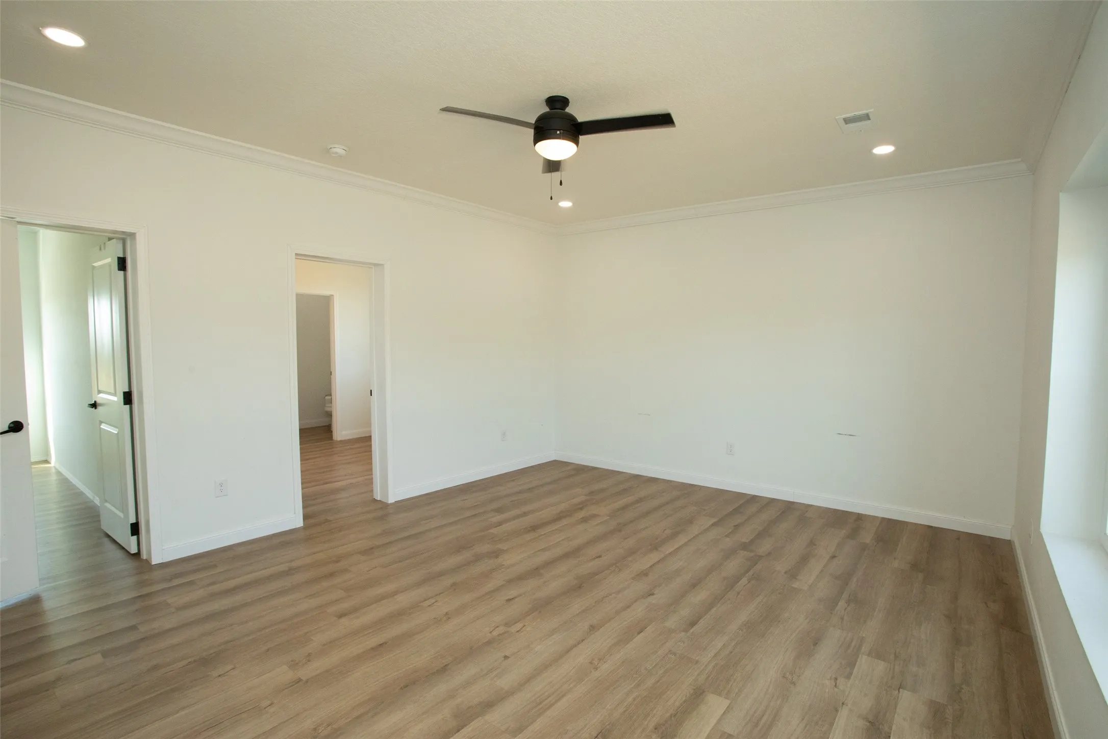 Spacious room featuring wood-finish flooring, crown molding, a ceiling fan with integrated lighting, and recessed lighting
