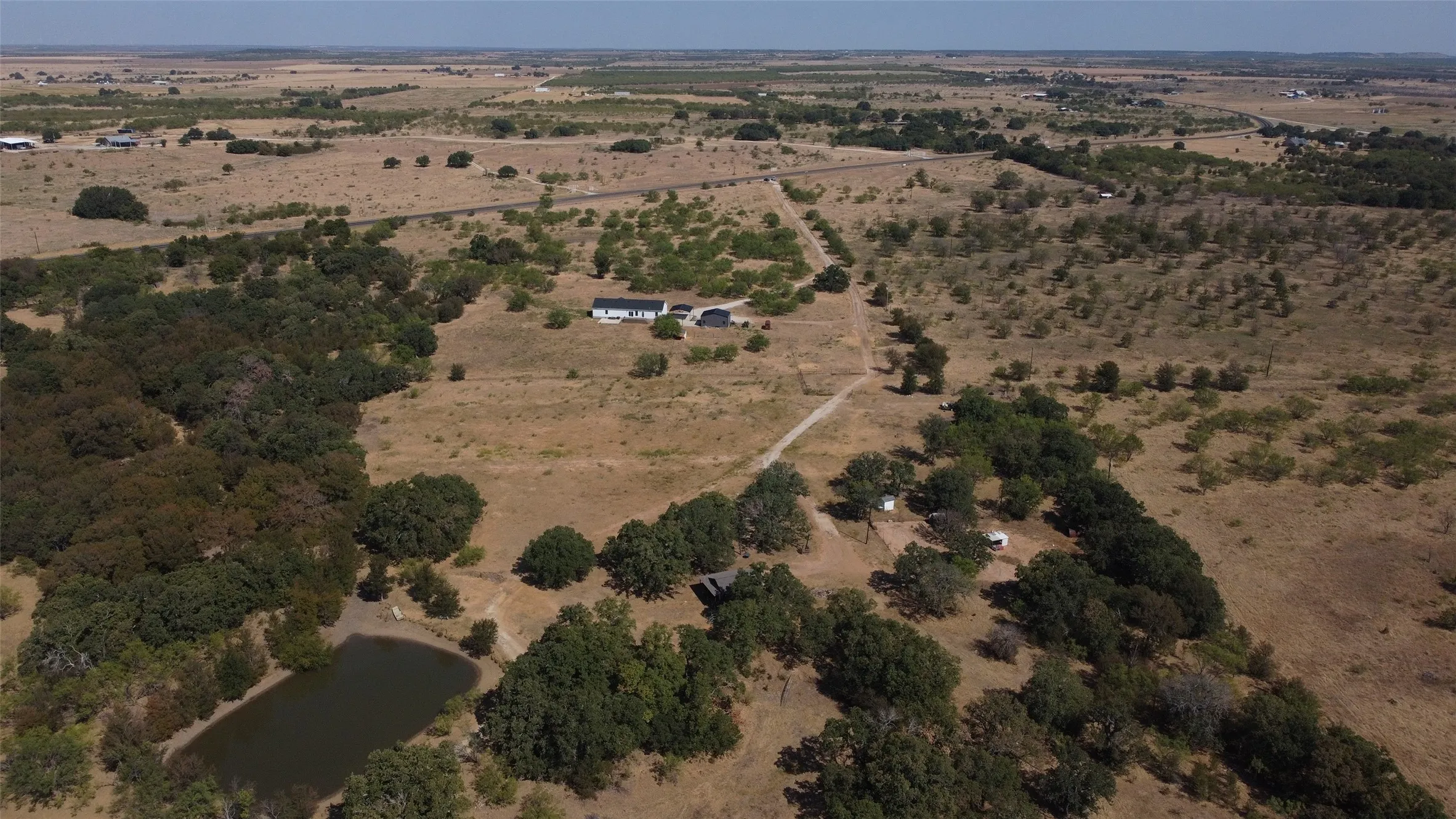 Expansive acreage featuring mature trees, open fields, a private pond, and a single-story residence