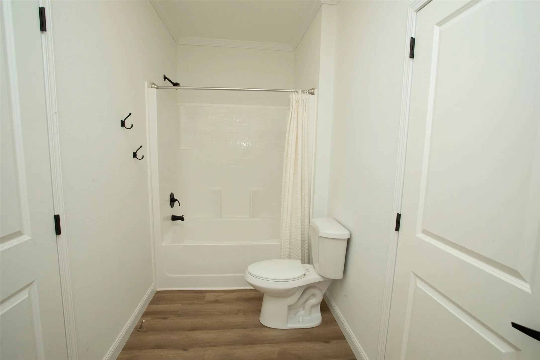 White tub/shower combination with black fixtures, wood-finish flooring, and white walls