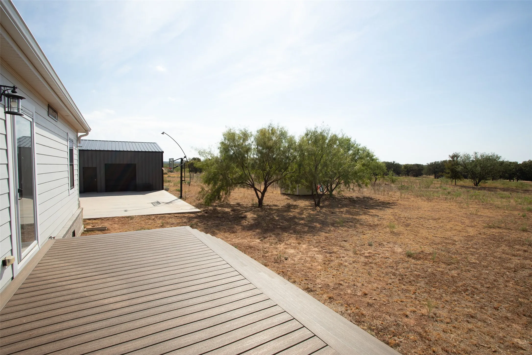 Expansive outdoor deck with wood-finish decking, detached metal structure, concrete pad, and mature trees