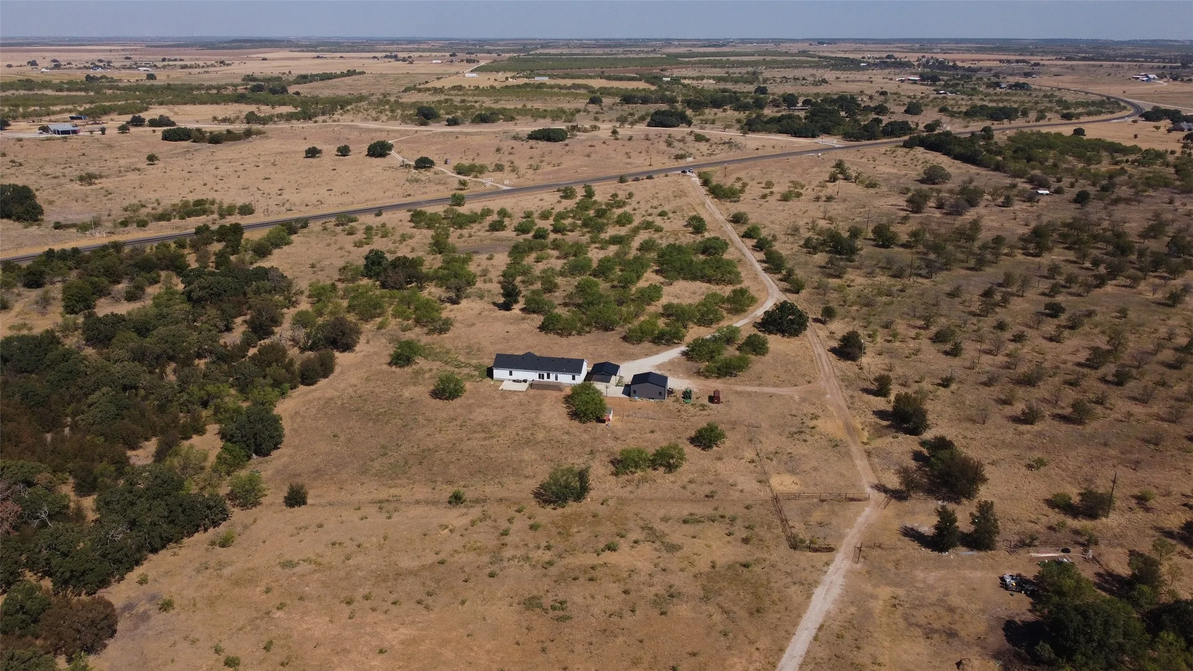 Expansive rural property featuring a single-story residence with a dark roof, surrounded by natural landscaping and mature trees
