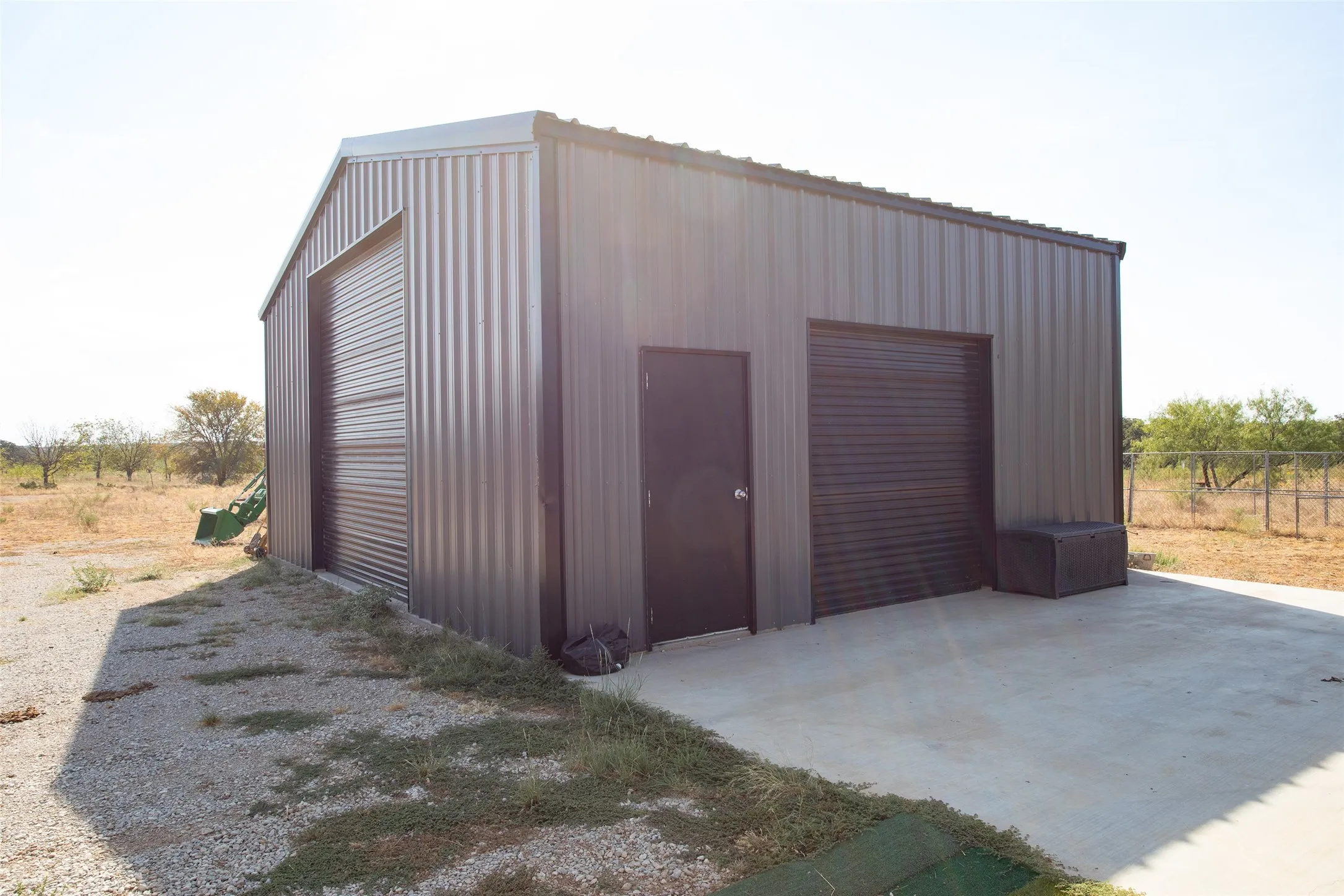 Corrugated metal structure featuring a gable roof, two roll-up doors, and a single entry door