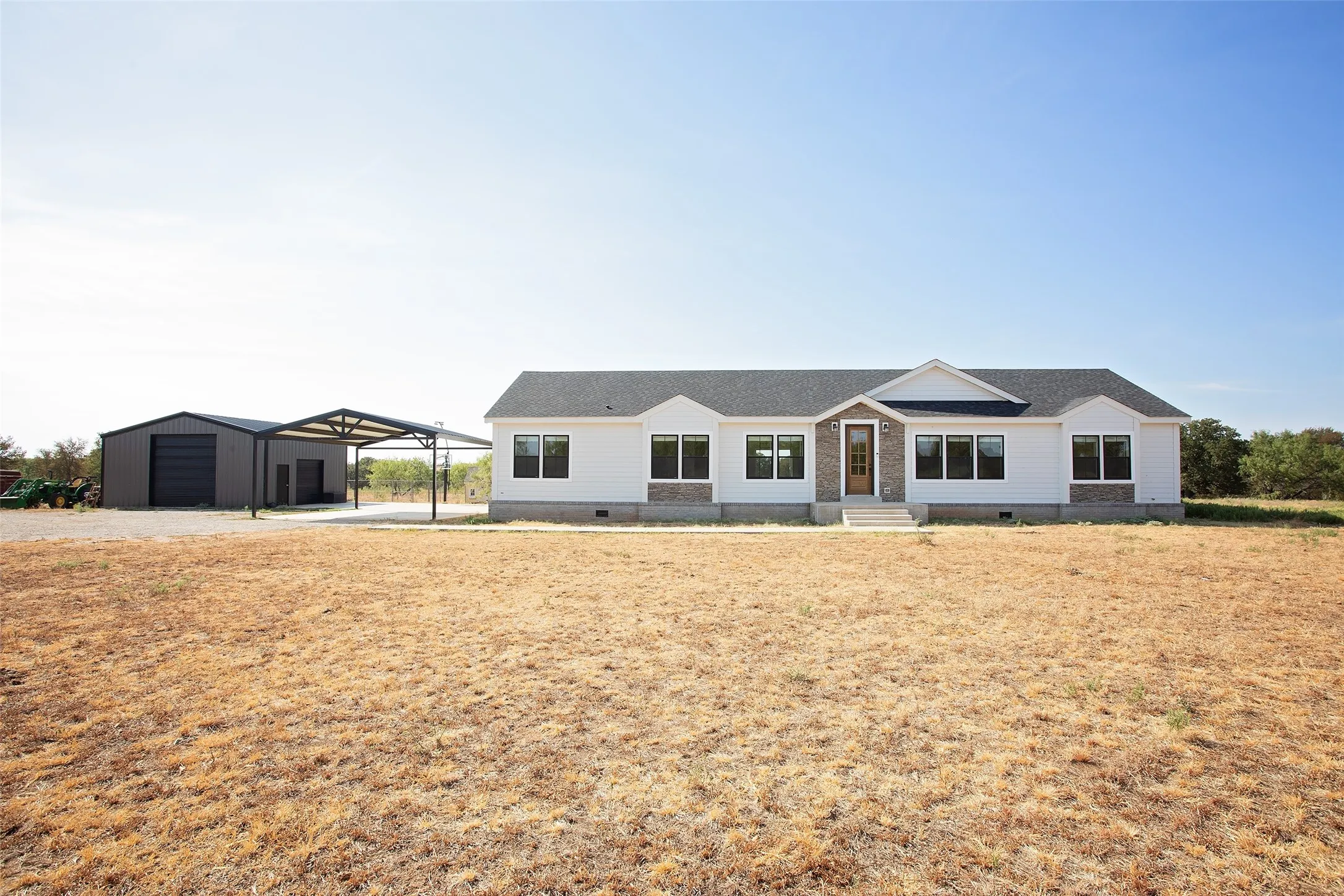 White siding exterior with stone accents, dark-framed windows, a covered front entry, a detached metal building, and a separate metal carport structure