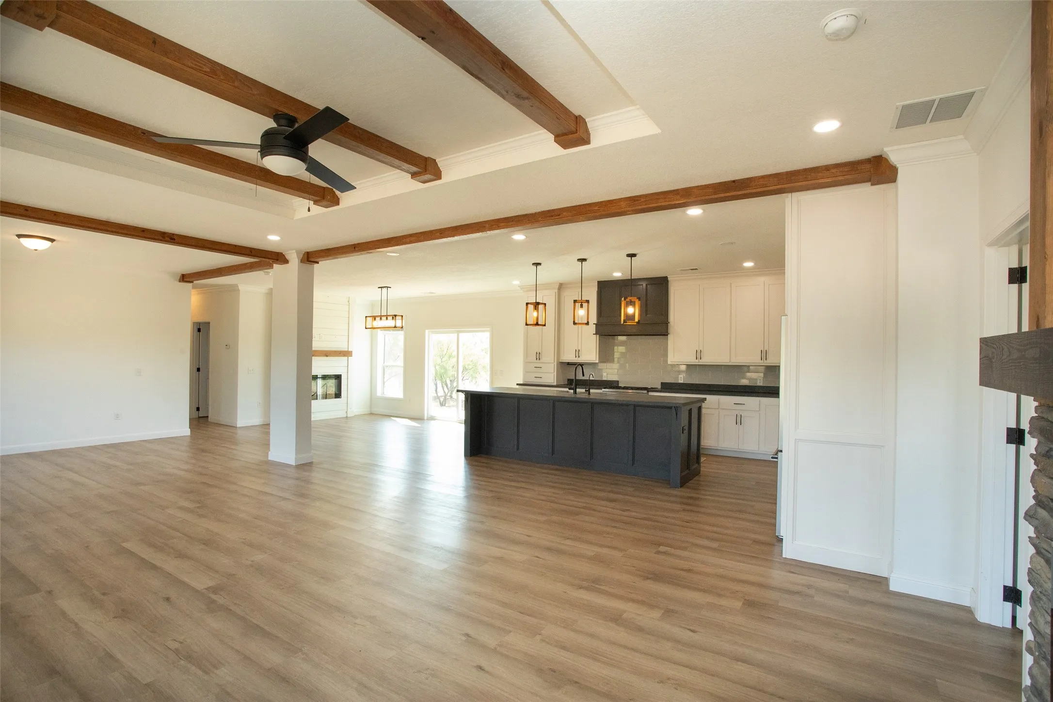 Open-concept living space with wood-finish flooring, exposed ceiling beams, recessed lighting, and a contemporary ceiling fan