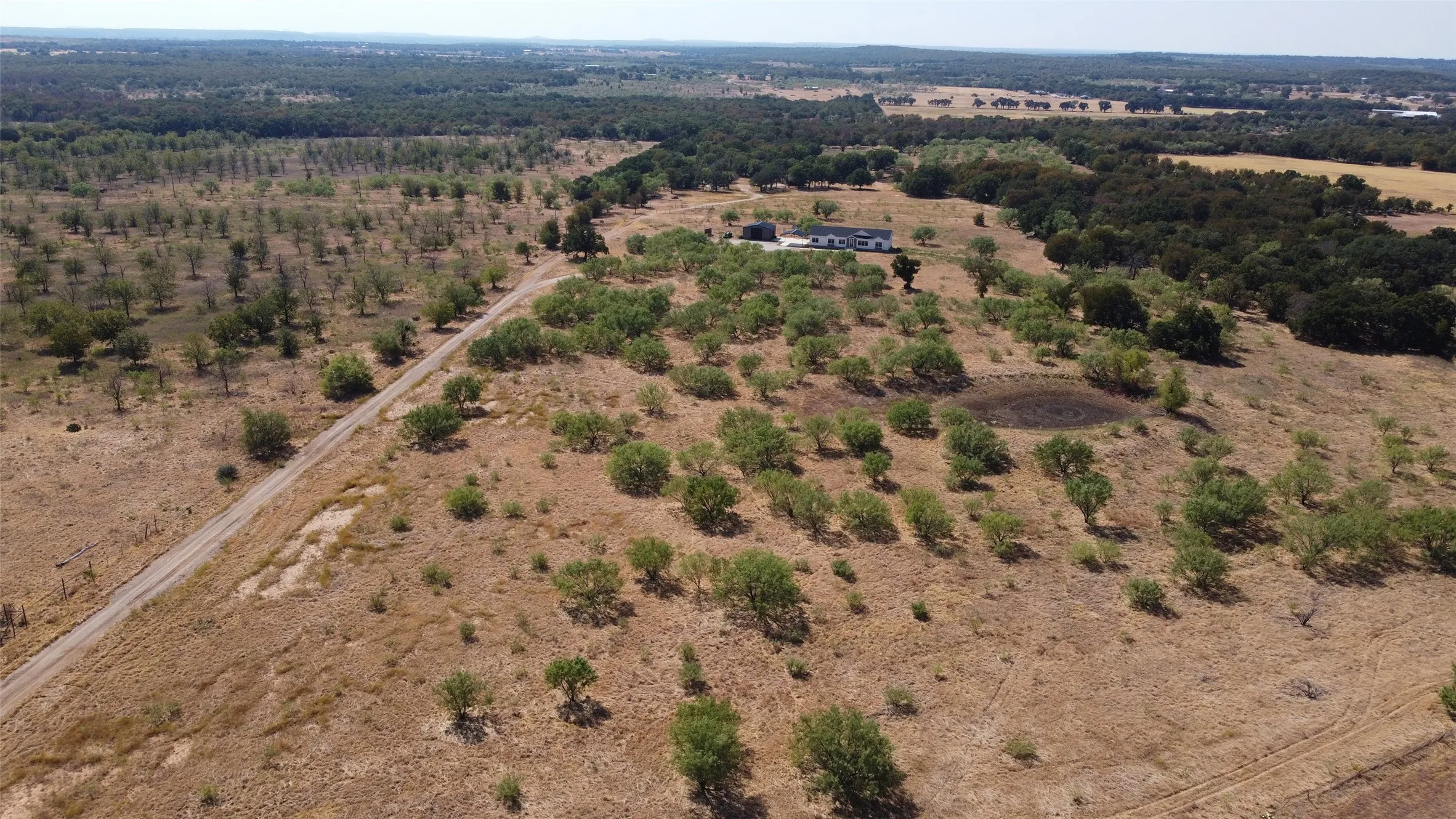 Expansive rural landscape featuring a single-story residence, a private road, and varied tree coverage