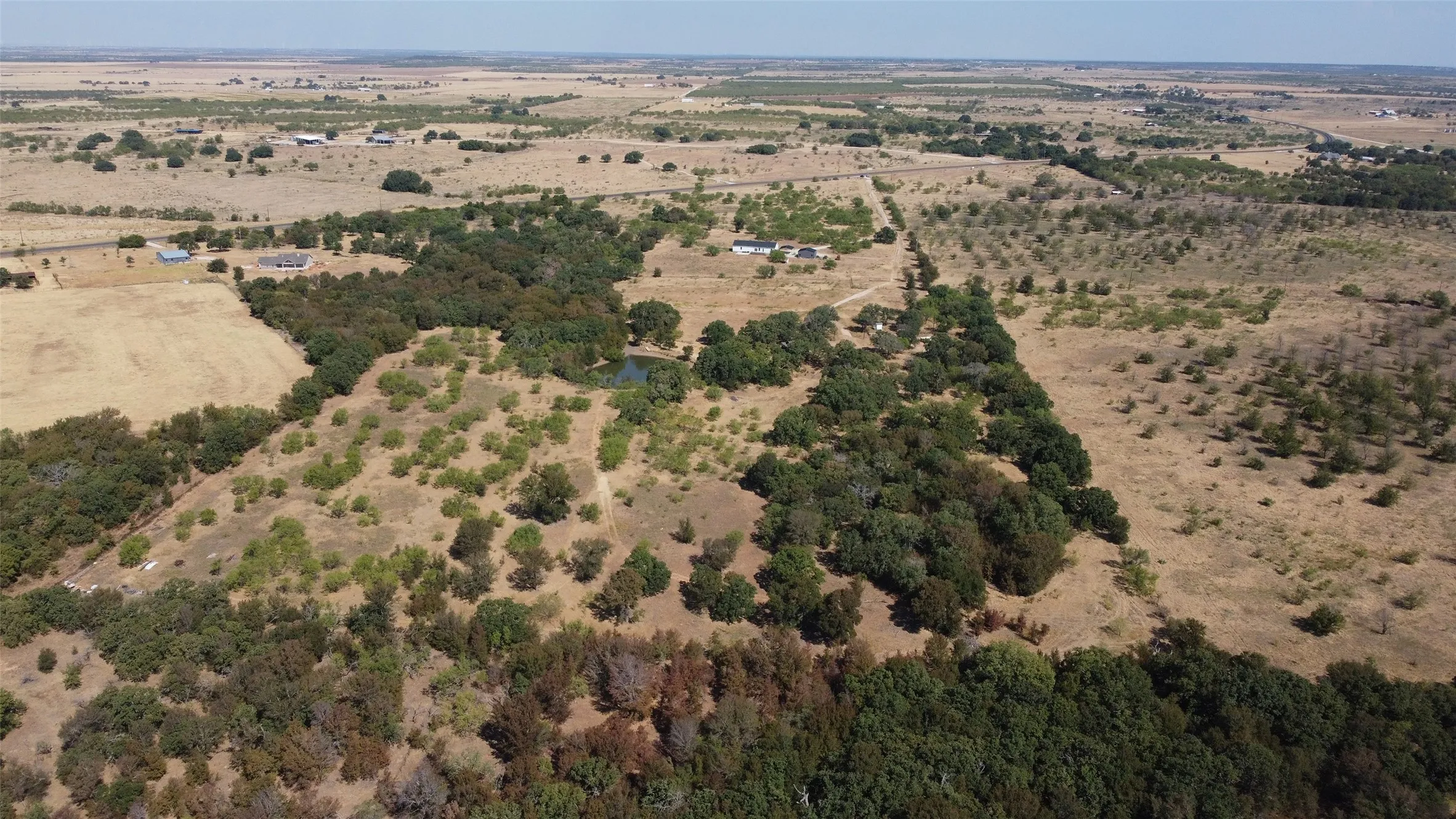Expansive land parcel featuring dense tree coverage, open fields, and a small pond