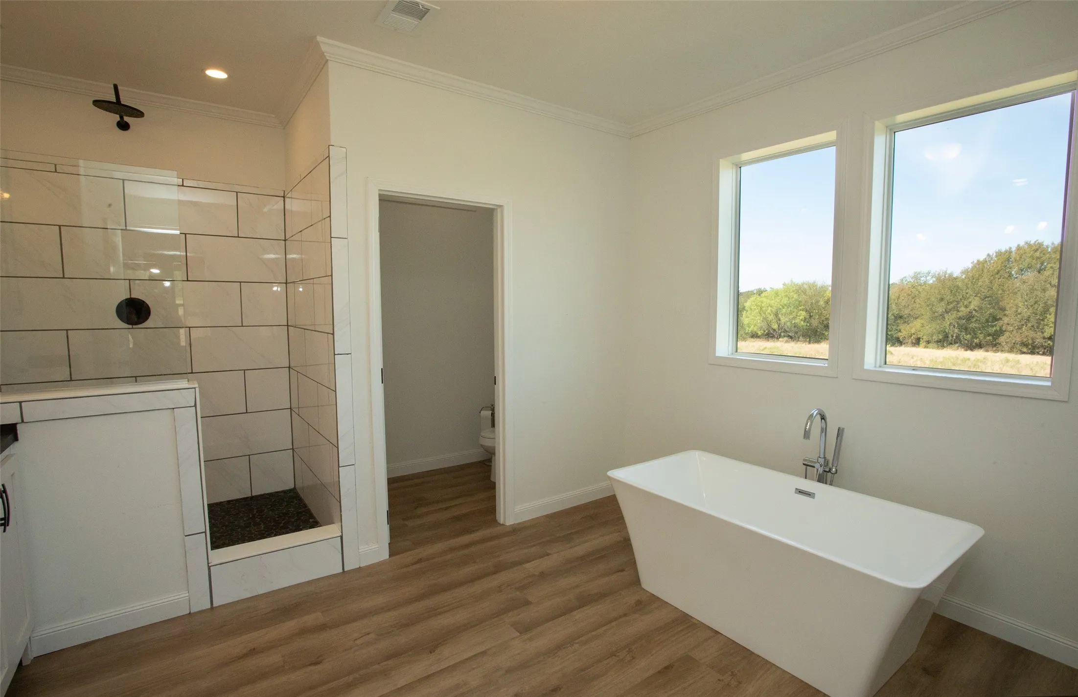 Freestanding soaking tub with chrome fixtures, wood-finish flooring, and two elongated windows