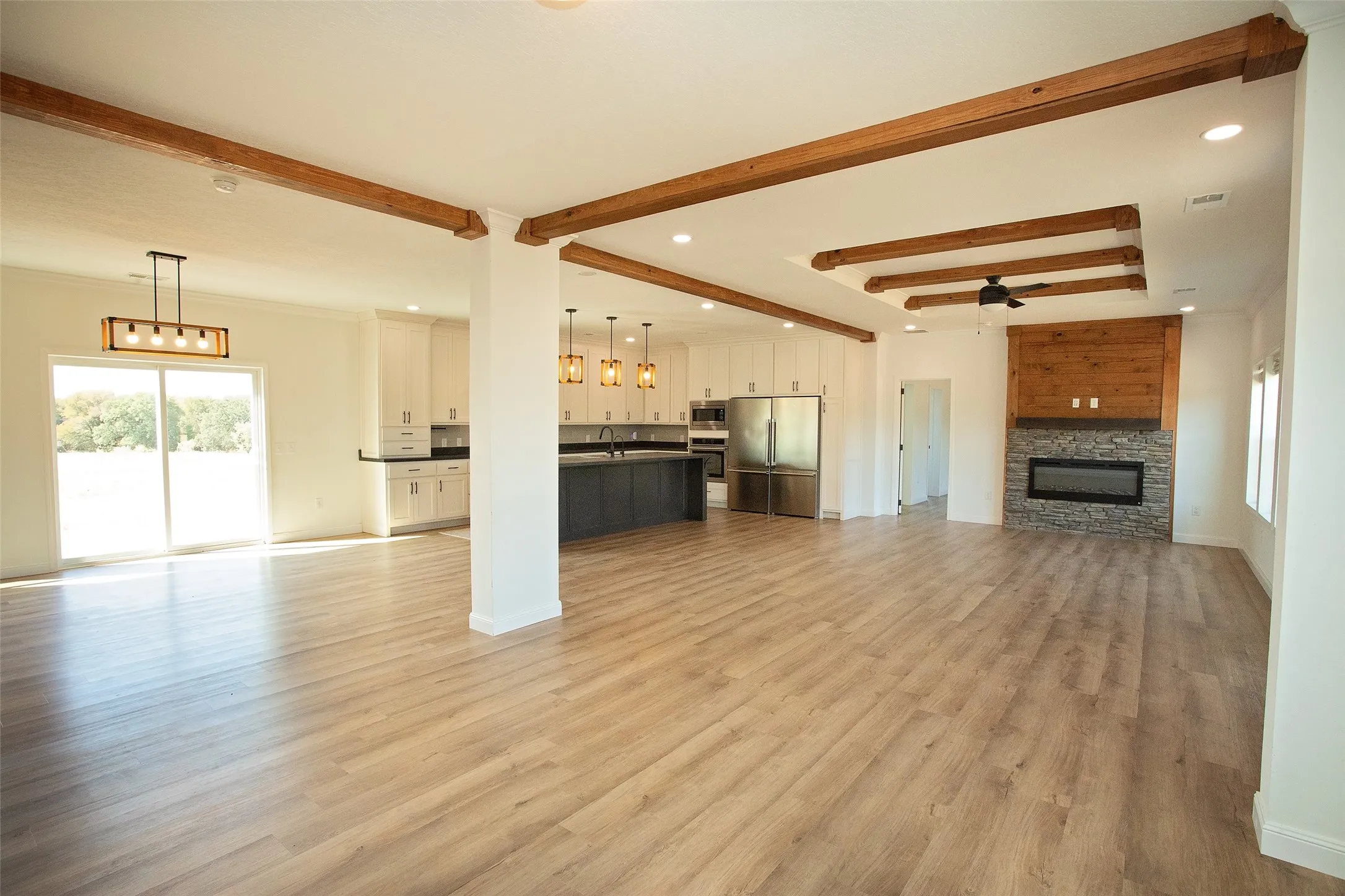 Wood-finish flooring, exposed wood beams, built-in electric fireplace with stone surround and wood paneling, white cabinetry, and stainless steel refrigerator