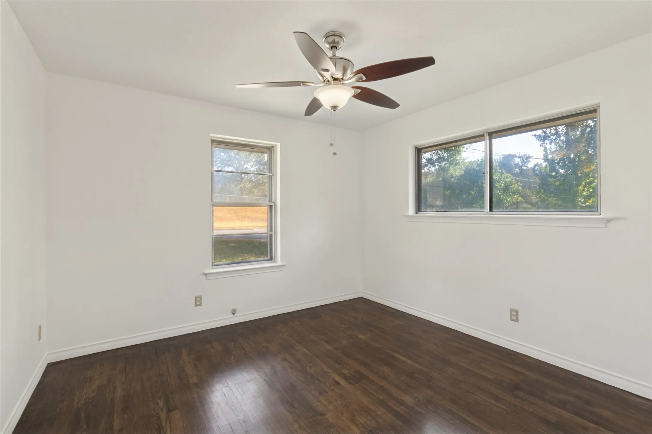 Wood-finish flooring, two windows, and a ceiling fan with integrated lighting