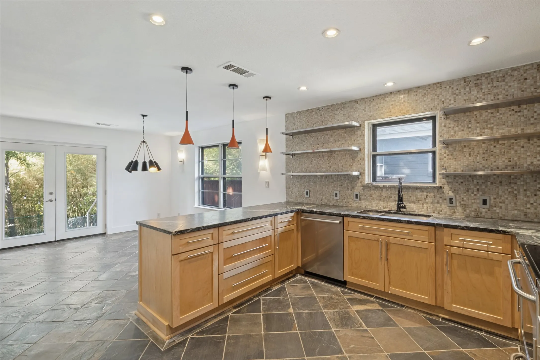 Kitchen featuring light wood-finish cabinetry, dark stone countertops, mosaic tile backsplash, and stainless-steel appliances