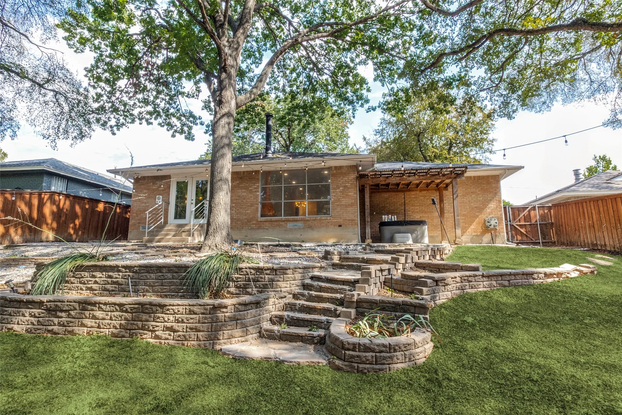 Brick exterior with a covered patio, terraced landscaping, stone retaining walls, and a grassy lawn