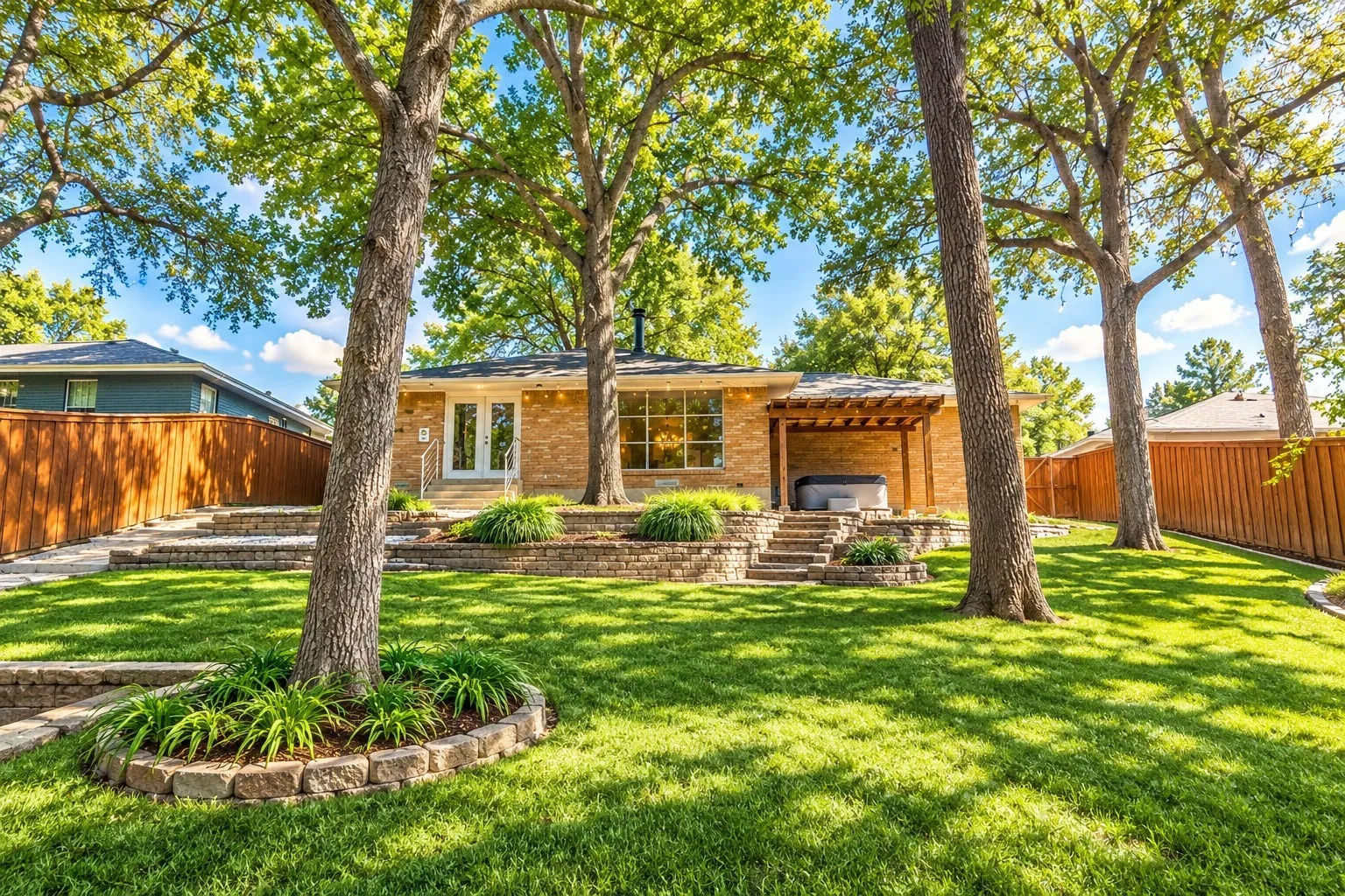 Digitally enhanced - Expansive backyard featuring a manicured lawn, mature trees, and a tiered hardscape design with stone retaining walls