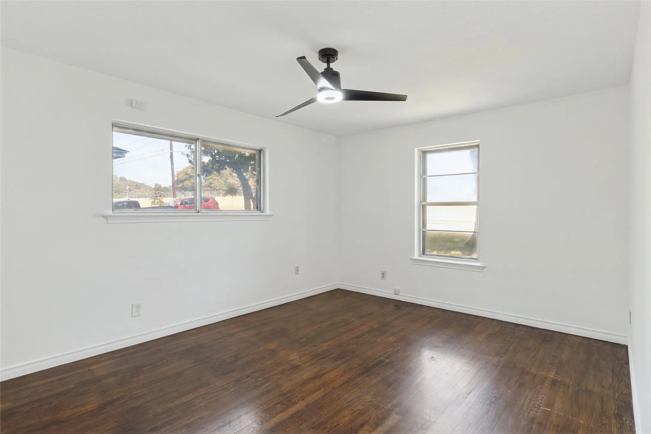 Spacious room with dark wood-finish flooring, white walls, and a contemporary ceiling fan