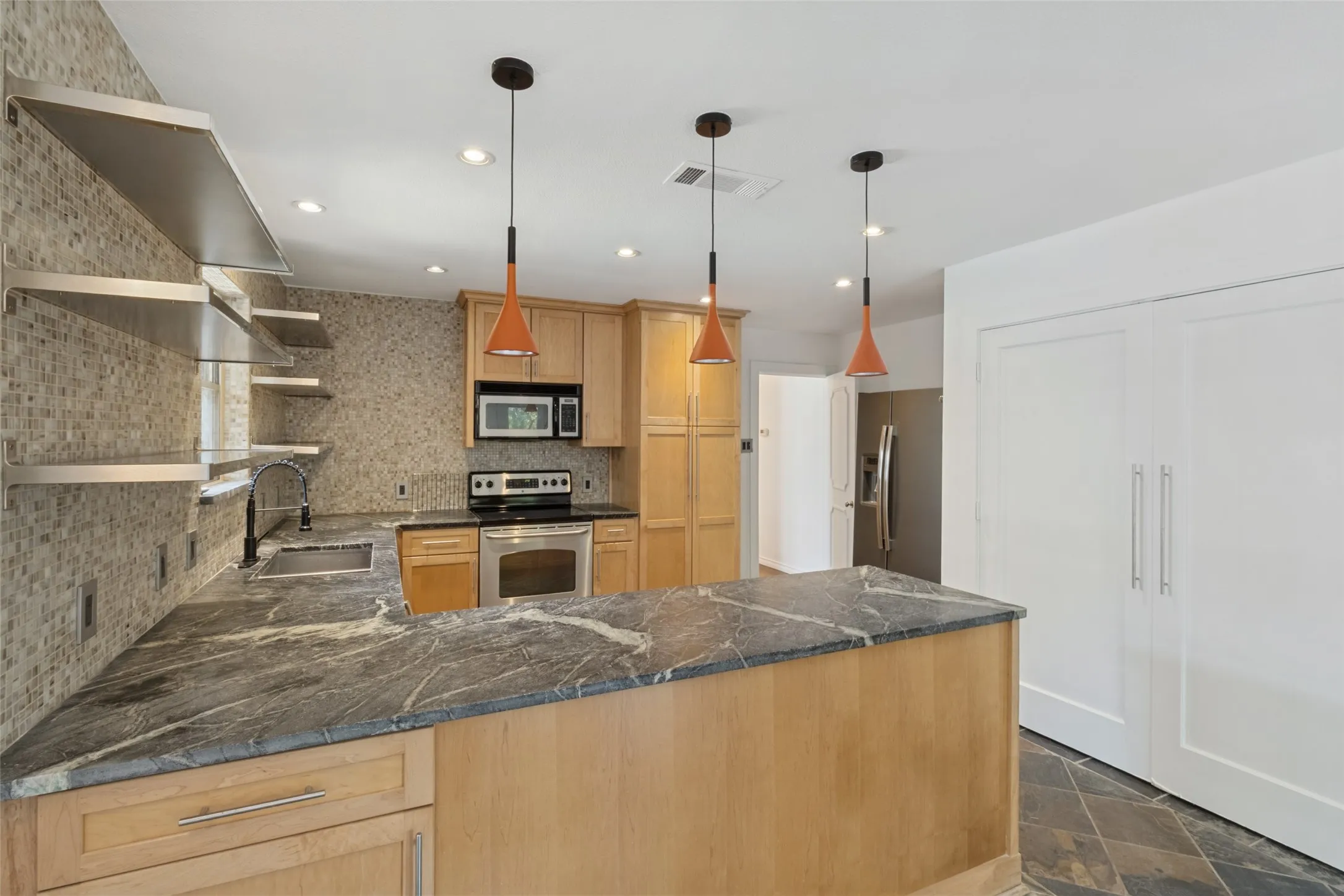Kitchen featuring natural wood cabinetry, dark-toned countertops, stainless steel appliances, and a mosaic tile backsplash